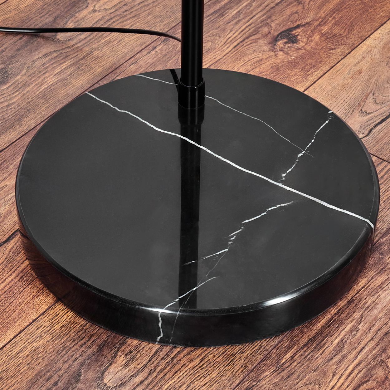 Ein schwarzer Marmorlampensockel mit weißen Adern steht auf einem Holzboden. Eine schwarze Stange ragt aus dem Sockel. Ein schwarzes Kabel ist sichtbar.