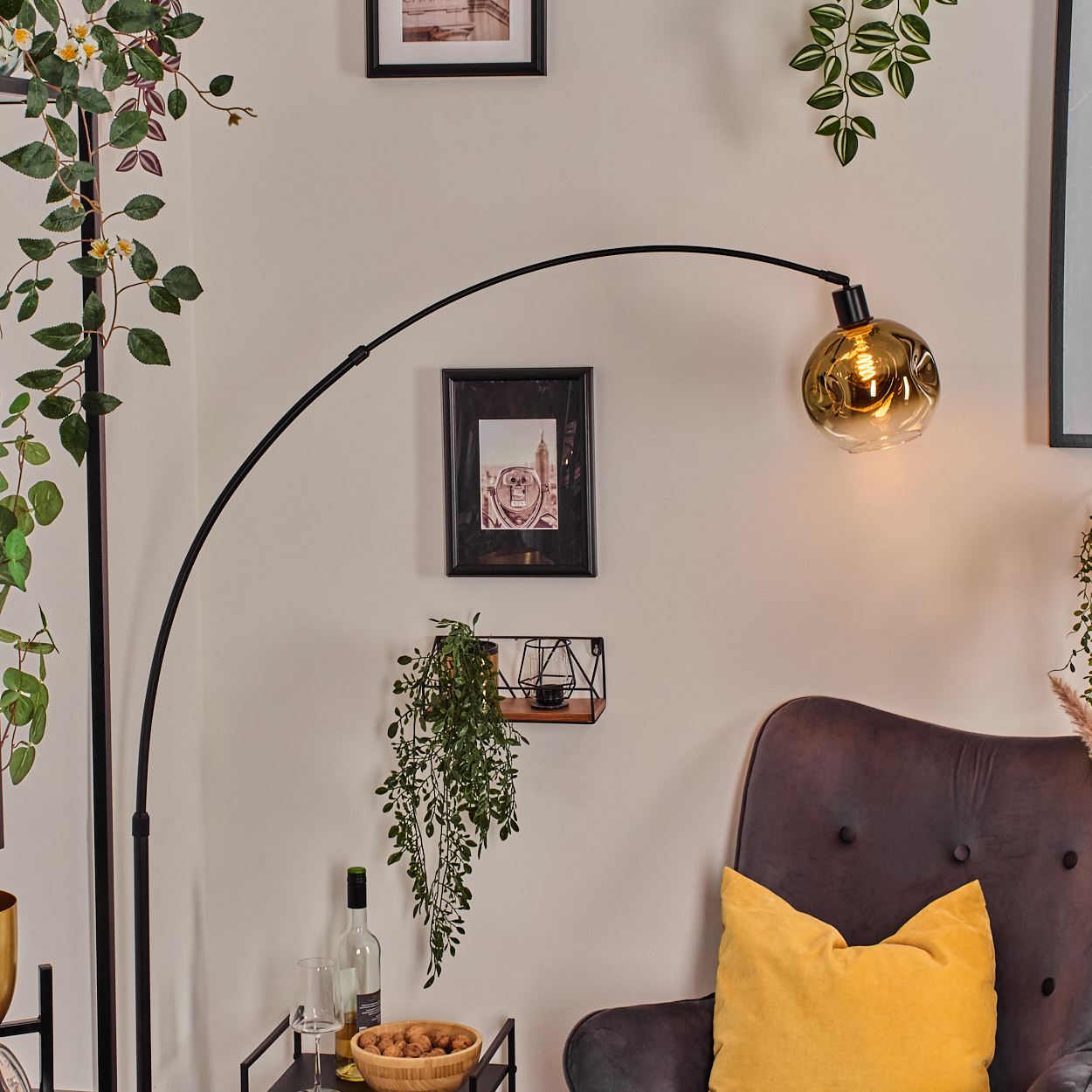 Ein modernes Wohnzimmer mit einer schwarzen Bogenlampe, einem grauen Sessel mit gelbem Kissen und gerahmten Bildern.