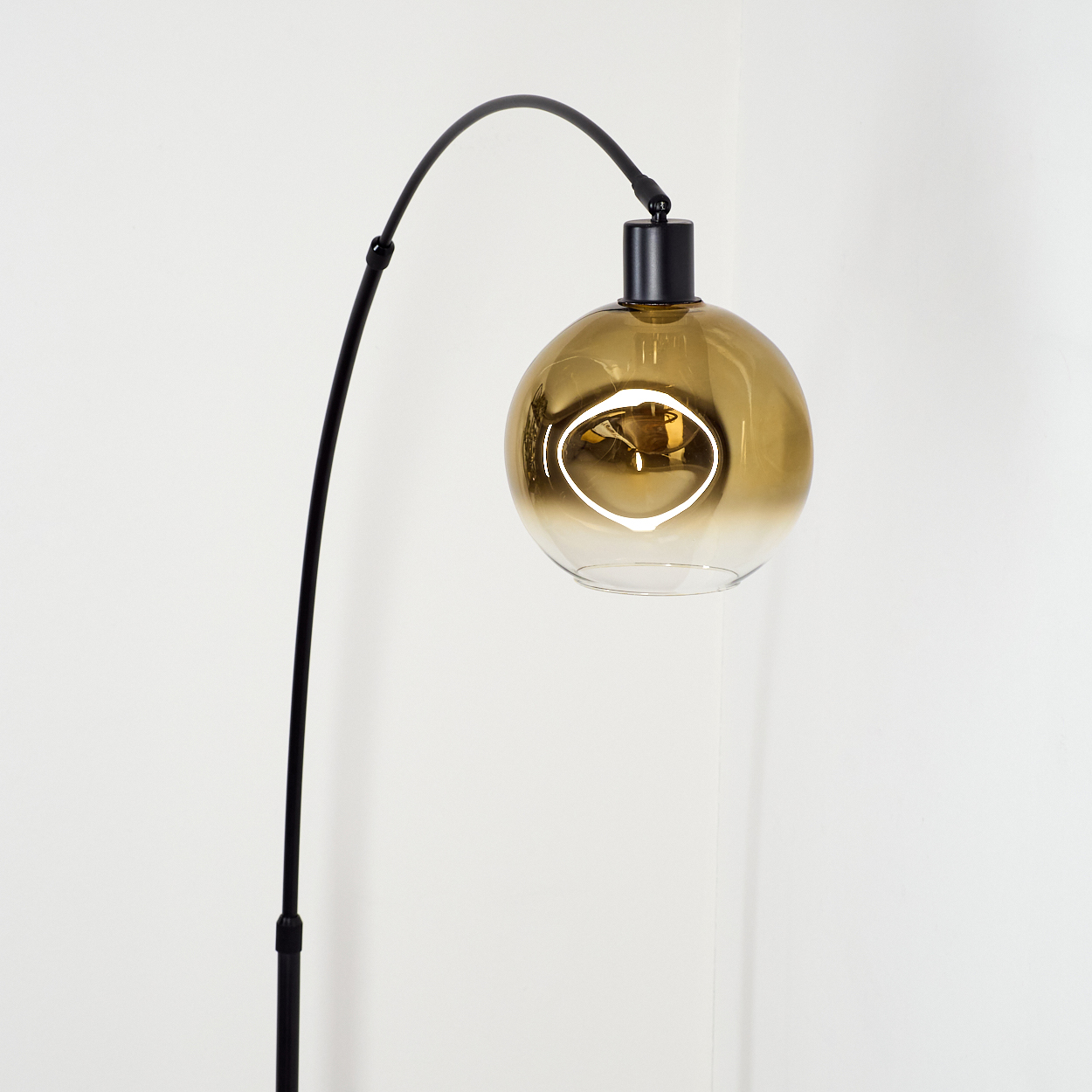 Eine moderne schwarze Stehlampe mit goldenem Glaskugelschirm. Der Hintergrund ist eine weiße Wand.