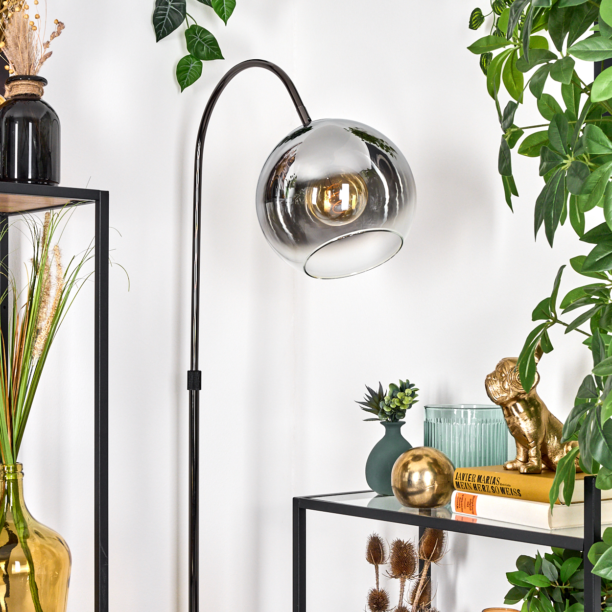 Eine moderne Lampe mit kugelförmigem Schirm. Dekorative Gegenstände auf Regalen, darunter Pflanzen, Vasen und eine goldene Bulldoggenstatue.