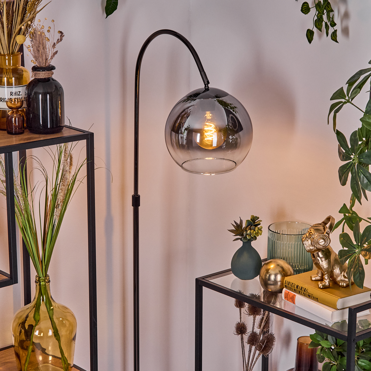 Eine moderne Innenszene mit Stehlampe, Dekoration auf Regalen und Pflanzen. Eine goldene Bulldoggenstatue steht auf einem Buch.