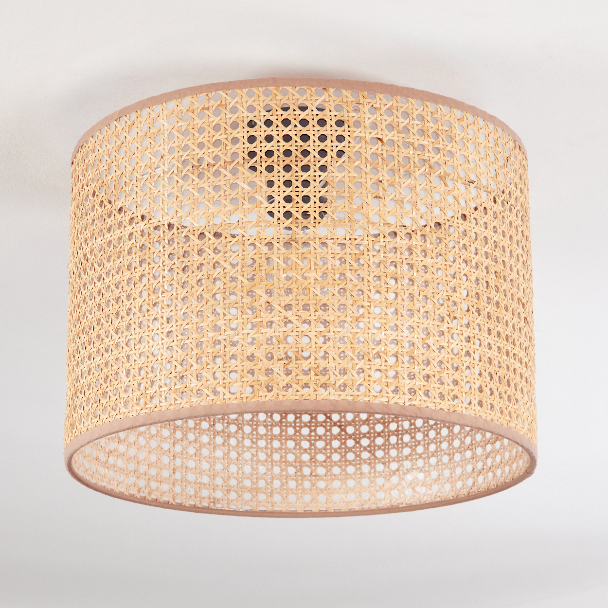 Ein zylindrischer Lampenschirm aus gewebtem Rattan mit hellbraunem Besatz. Der Hintergrund ist eine weiße Decke.