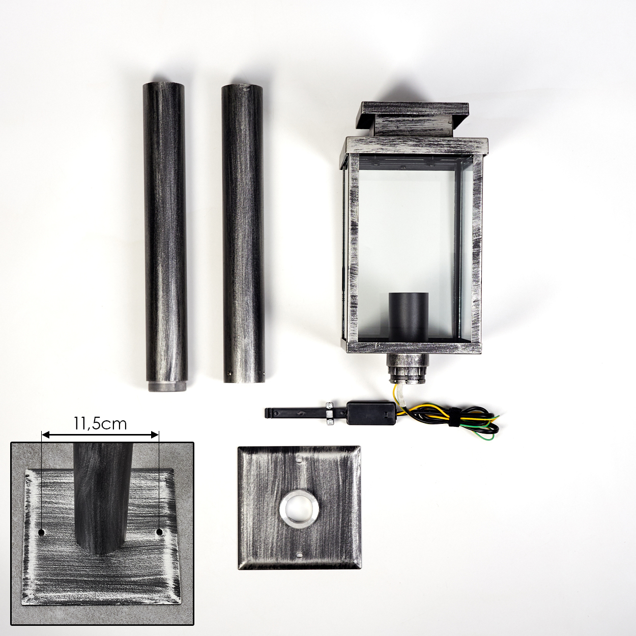 Bestandteile einer Lampe auf weißer Oberfläche: zwei Metallstangen, eine quadratische Basis, eine Lampe und Kabel. Die Lampe hat ein Glasgehäuse.