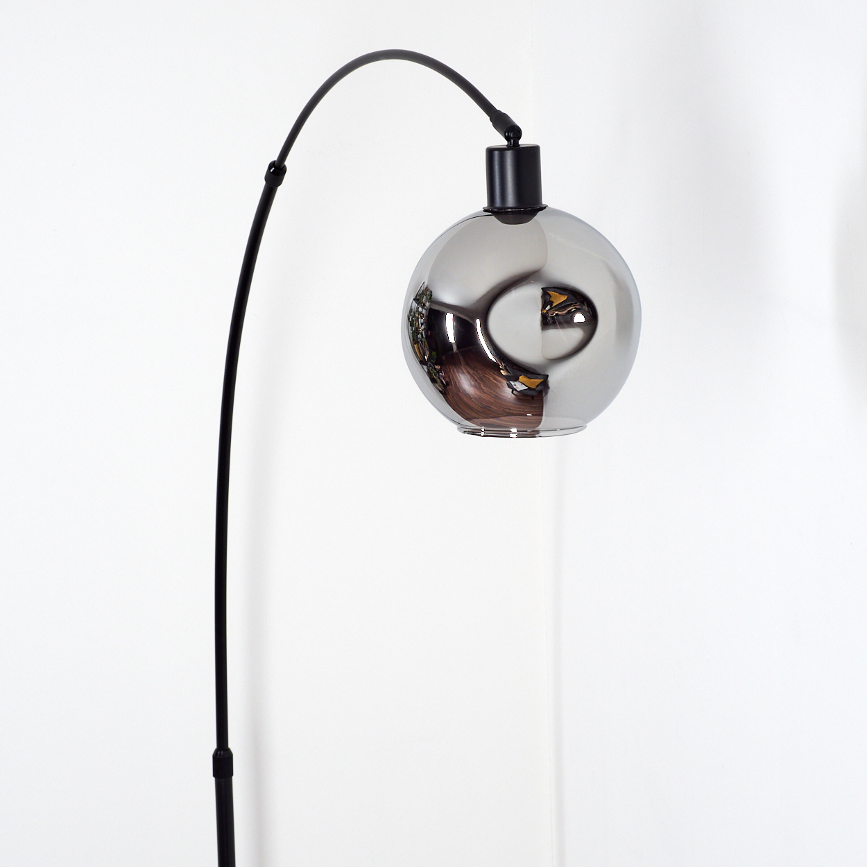 Eine moderne Stehlampe mit schwarzem, gebogenem Stiel und großem, reflektierendem, silberfarbenem Globus-Schirm. Weißer Hintergrund.