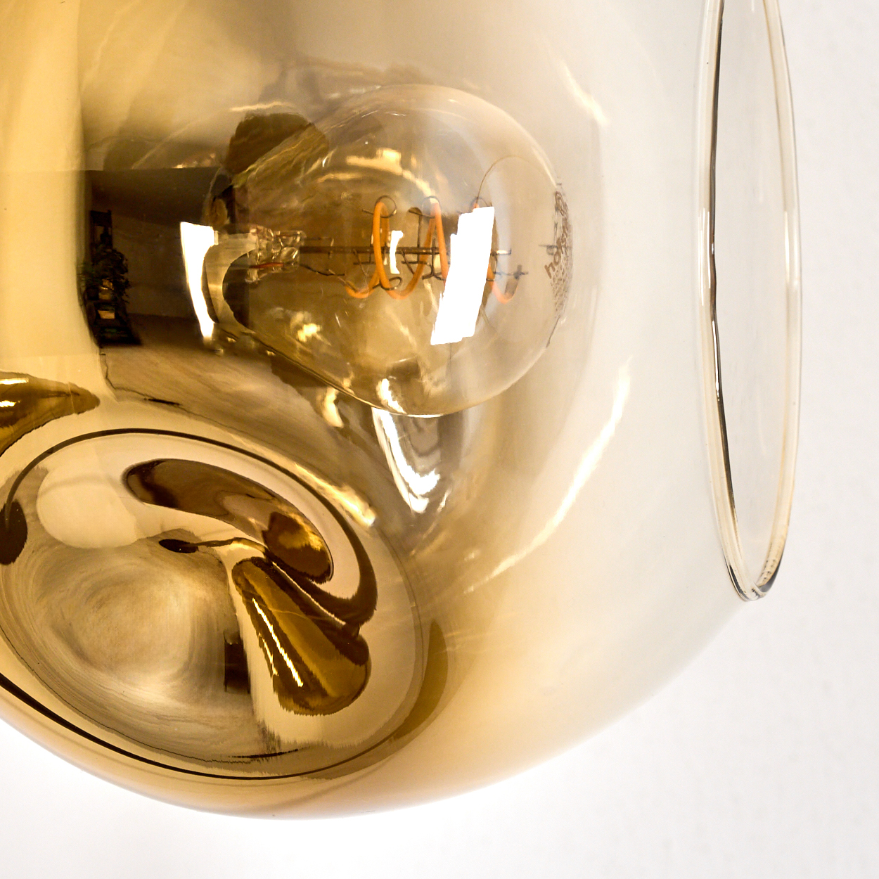 Nahaufnahme einer Glühbirne in einem goldenen, transparenten Glasschirm. Die Glühbirne hat einen sichtbaren orangefarbenen Glühfaden.