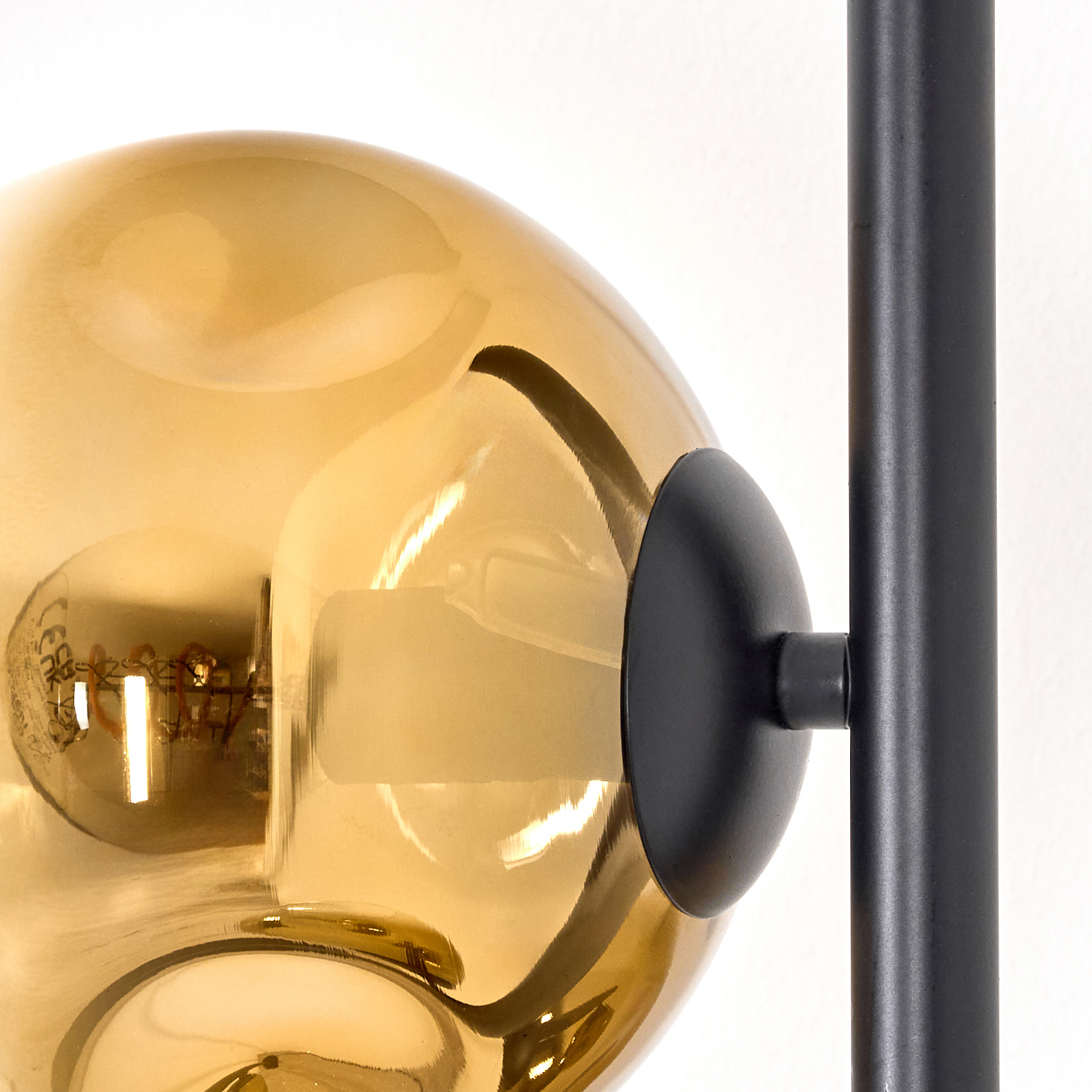 Nahaufnahme eines goldenen Glasschirms, eines schwarzen Metallrahmens und einer sichtbaren Glühbirne im Inneren.