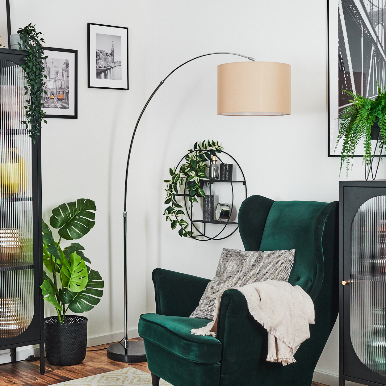 Ein grüner Sessel mit Decke und Kissen, eine Stehlampe, eine Pflanze und schwarz gerahmte Bilder hängen an einer weißen Wand.