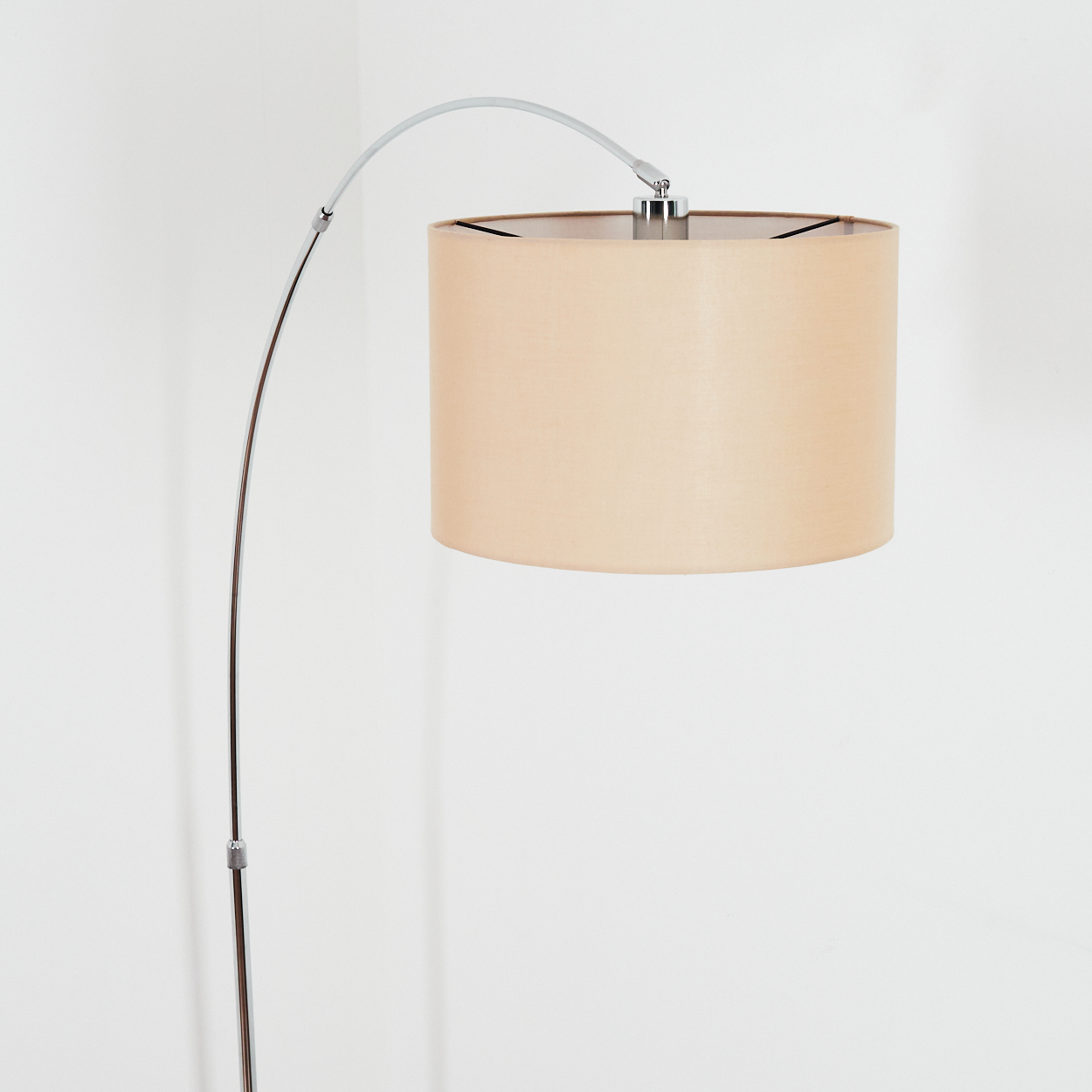 Eine moderne Stehlampe mit beigem Lampenschirm. Die Lampe hat einen gebogenen Chromarm und steht vor einer weißen Wand.