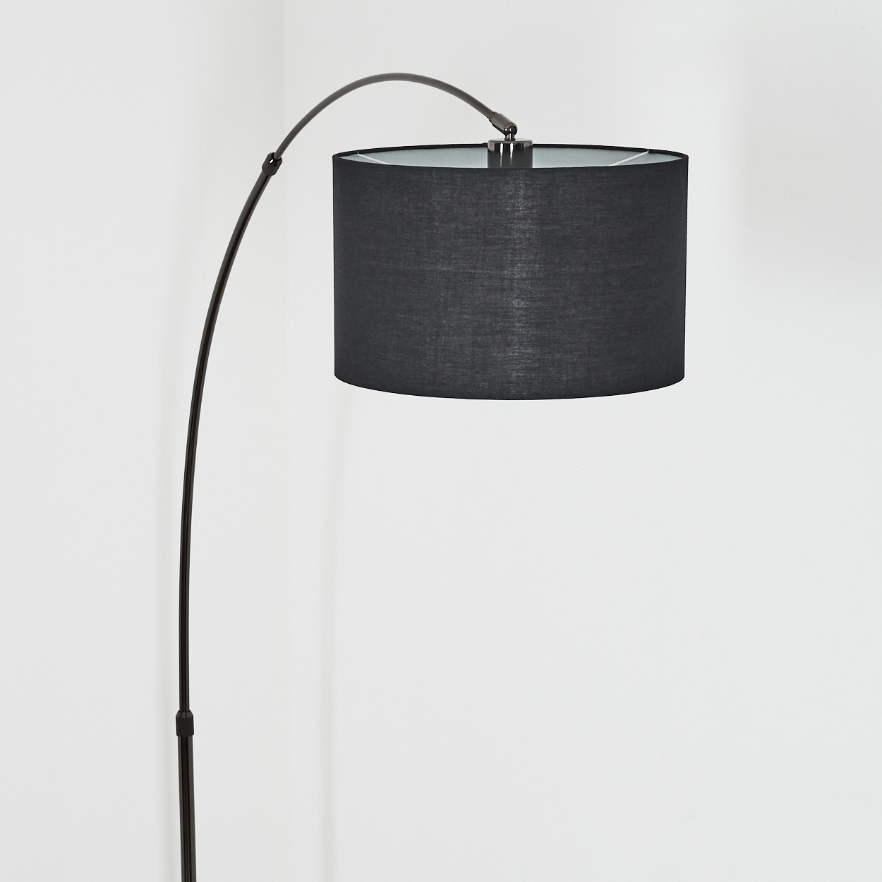 Eine moderne schwarze Bogen-Stehlampe vor einer weißen Wand. Die Lampe hat einen dunklen Schirm, auch der Fuß ist dunkel.