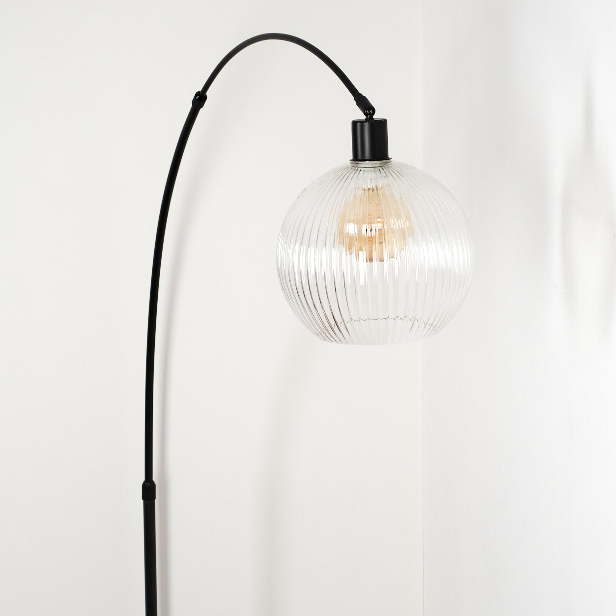 Eine moderne schwarze Lampe mit einem klaren, gerippten Glaskolben. Die Lampe steht vor einer weißen Wand.