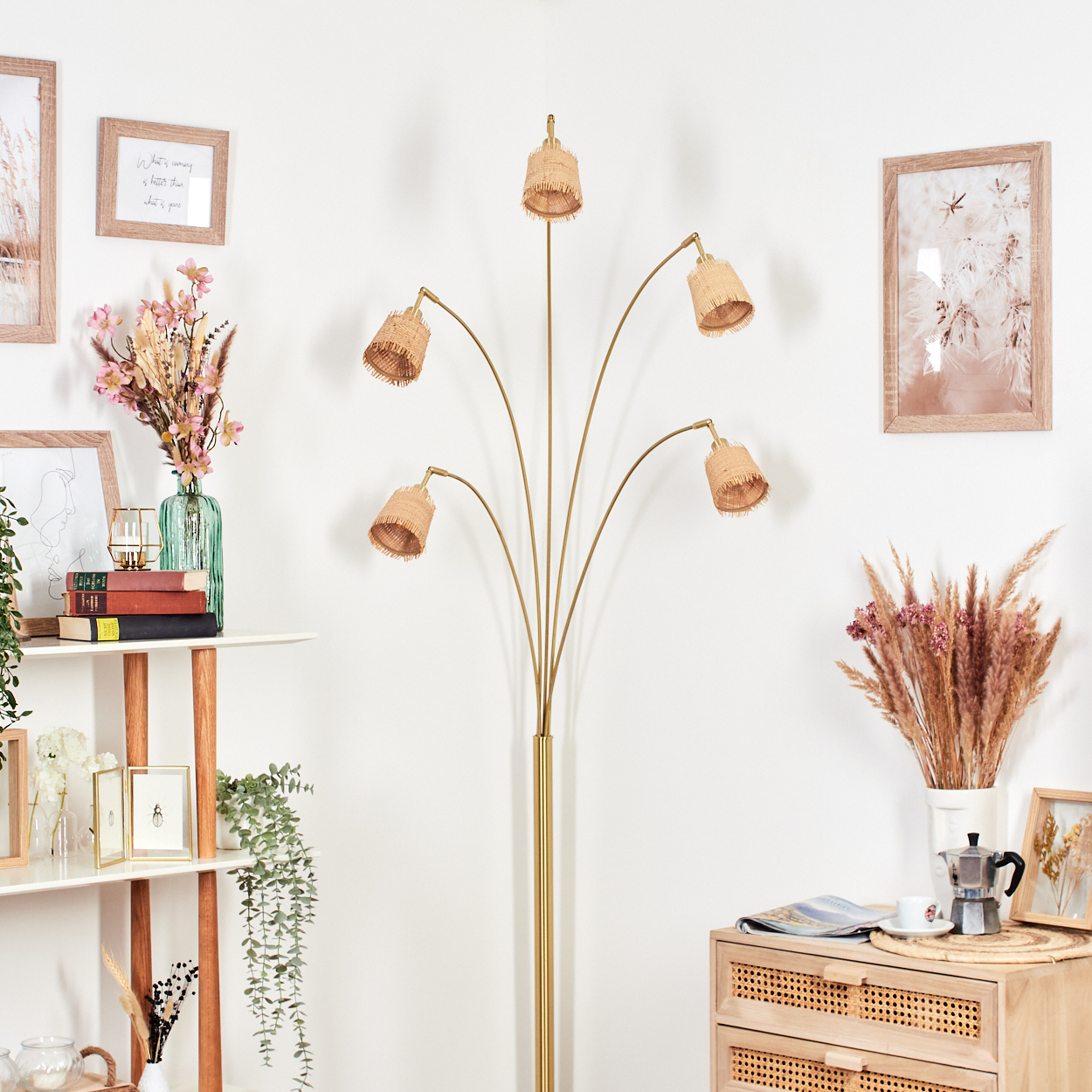 Eine goldene Stehlampe mit gewebten Schirmen steht vor einer weißen Wand. Andere Dekorationen umfassen Bilderrahmen und einen Beistelltisch.