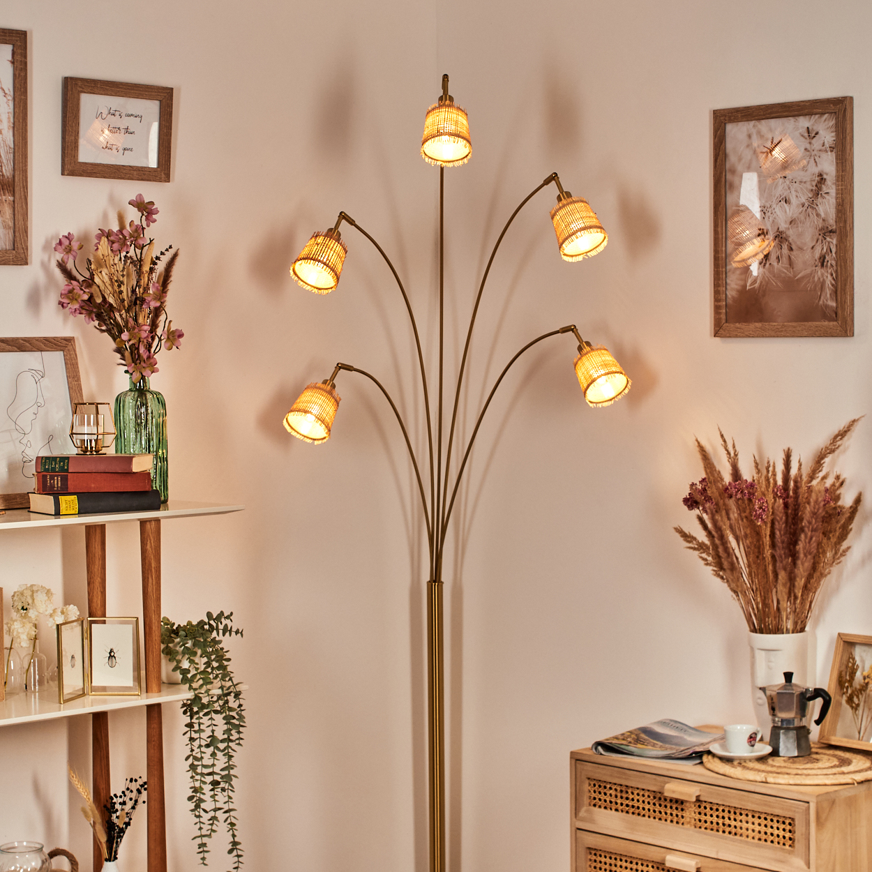 Eine Stehlampe mit fünf Lichtern, umgeben von Dekoration wie Bildern, Vasen mit Blumen und einem Holzschrank mit Kaffeemaschine.