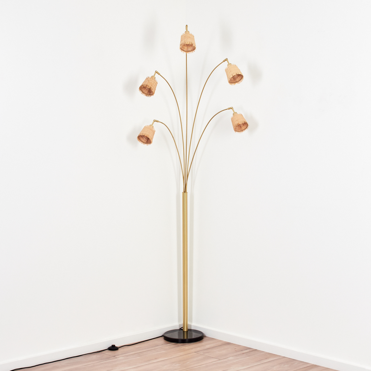 Eine goldene Stehlampe mit fünf Lampenschirmen. Die Lampe hat einen schwarzen Fuß, einen hohen Schaft und gebogene Arme mit den Lampenschirmen.