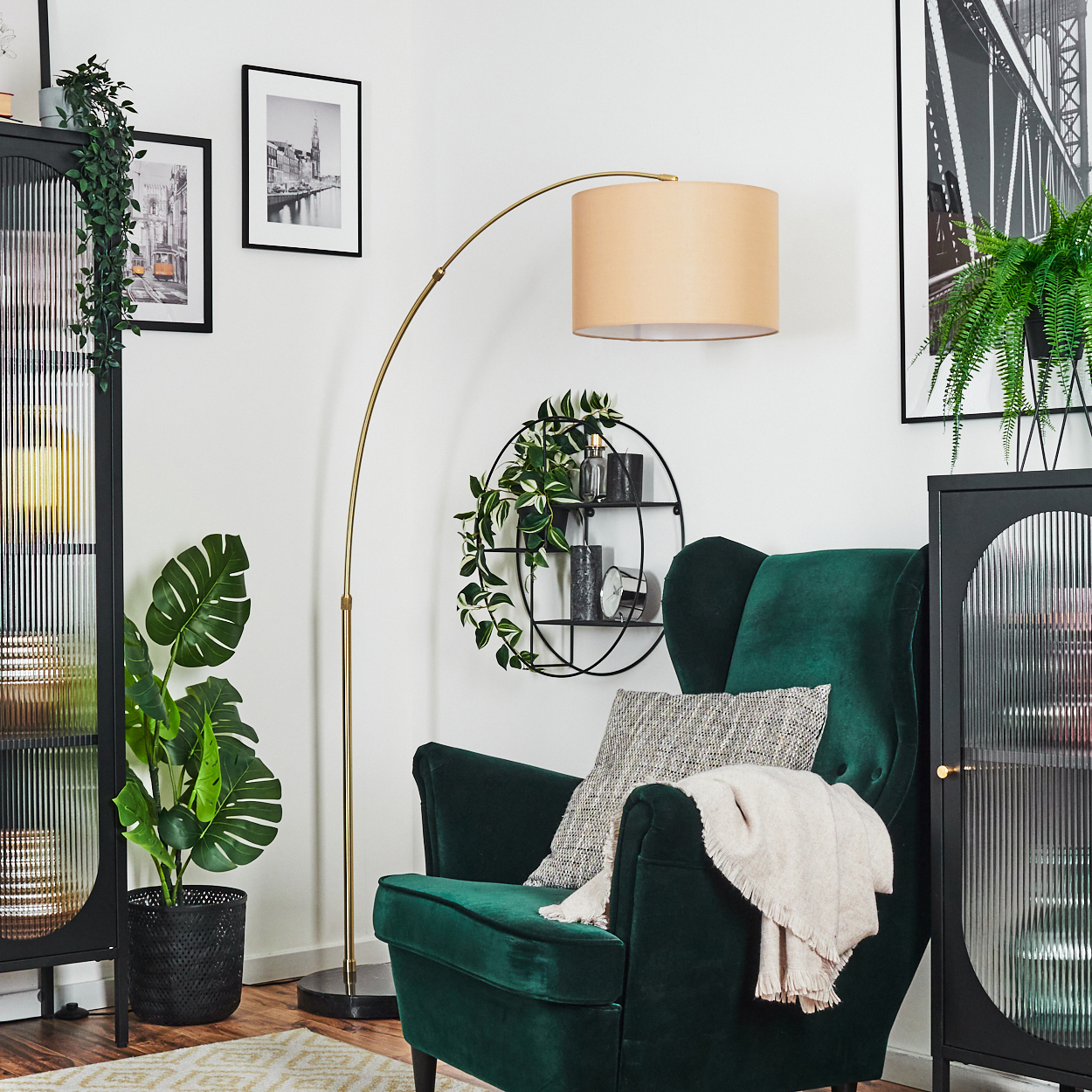 Ein grüner Sessel mit Decke und Kissen, eine Stehlampe und eine Pflanze in einem schwarzen Topf befinden sich in einem Raum.