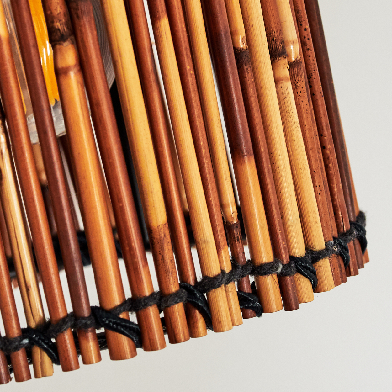 Nahaufnahme eines Lampenschirms aus Bambusstäben. Die Stäbe sind braun und beige, mit schwarzem Faden gebunden, vor weißem Hintergrund.