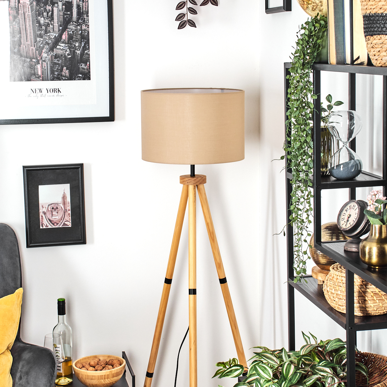 Ein Raum mit einer Holzlampe, einem schwarzen Regal mit Dekorationen und zwei gerahmten Bildern an der Wand. Auf einem Tisch steht eine Weinflasche.
