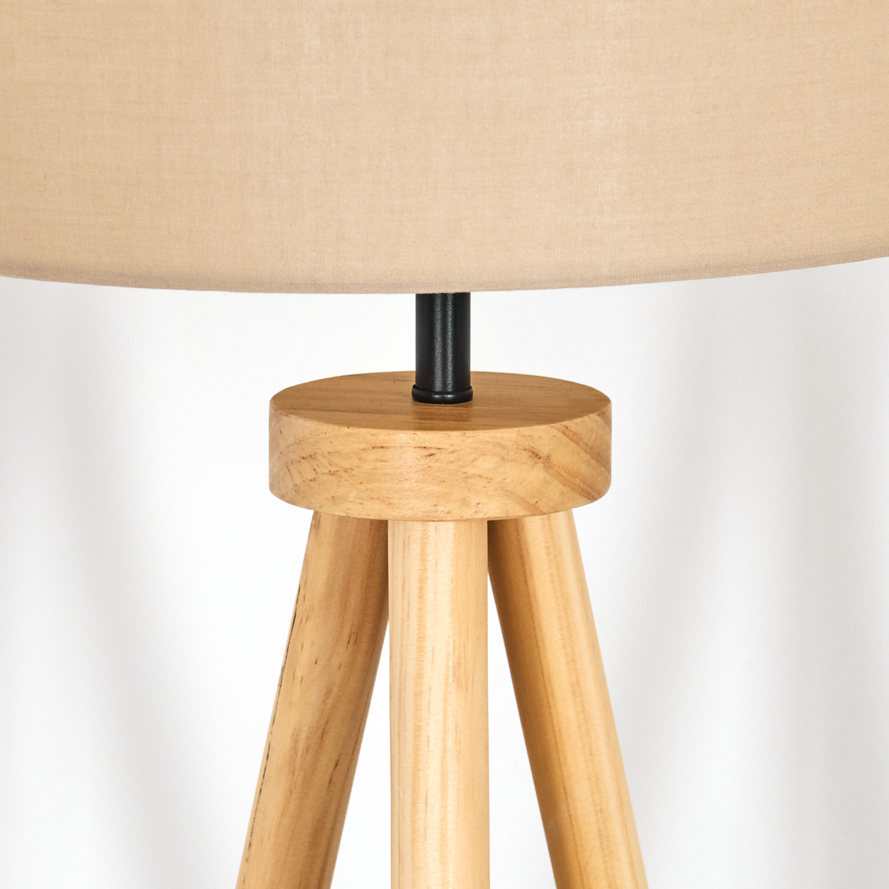 Ein beiger Lampenschirm sitzt auf einem hölzernen Stativfuß. Die Lampe hat eine schwarze Mittelsäule und Beine aus hellem Holz.