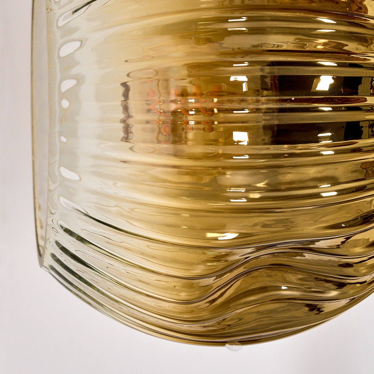 Nahaufnahme eines goldenen Glasobjekts mit wellenförmigen horizontalen Linien. Das Objekt reflektiert Licht. Weißer Hintergrund.