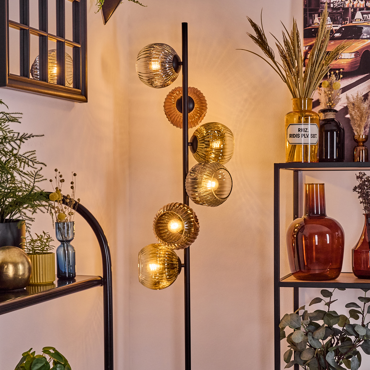 Eine moderne Stehlampe mit Glaskugelschirmen. Der Raum hat Regale mit Vasen und Pflanzen sowie eine Wand mit einem Poster.