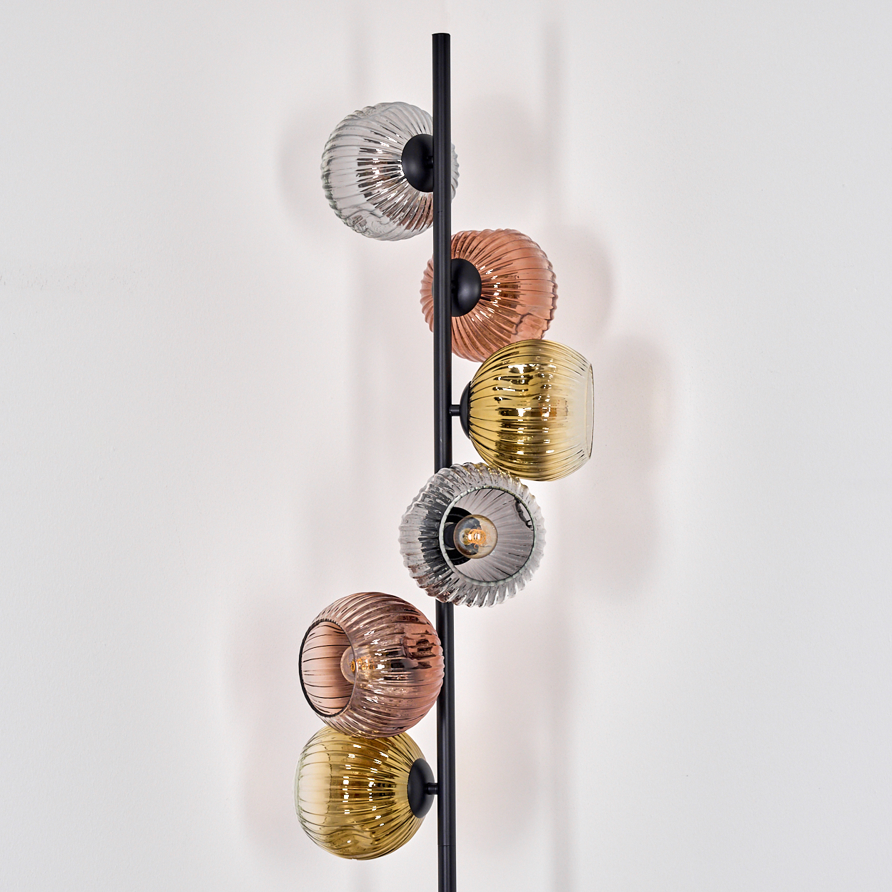 Eine moderne Wandlampe mit sechs bunten, gerippten Glaskugeln. Die Lampe hat einen schwarzen Metallrahmen an einer weißen Wand.