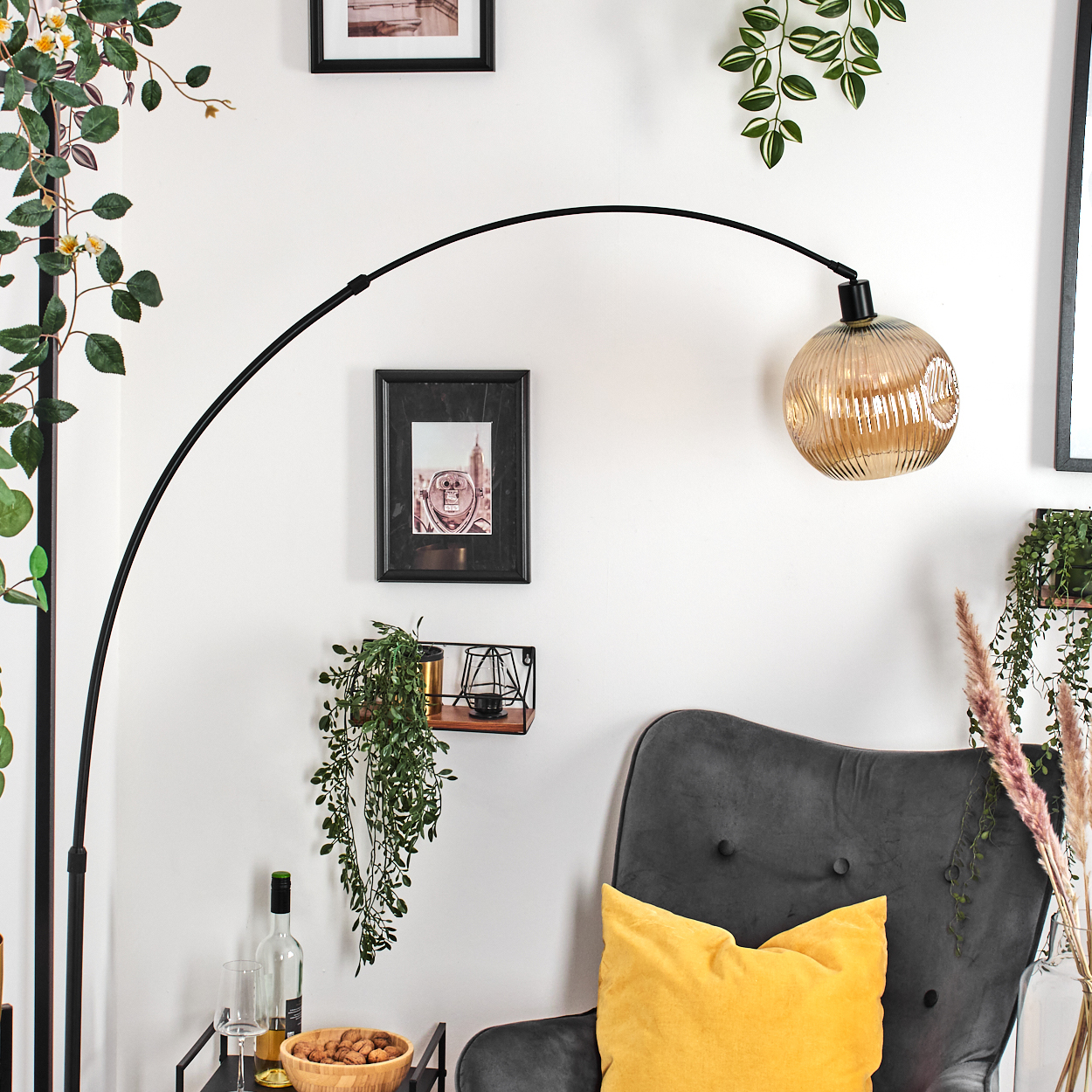 Ein modernes Wohnzimmer mit schwarzer Bogenlampe, grauem Sessel mit gelbem Kissen und Zierpflanzen.