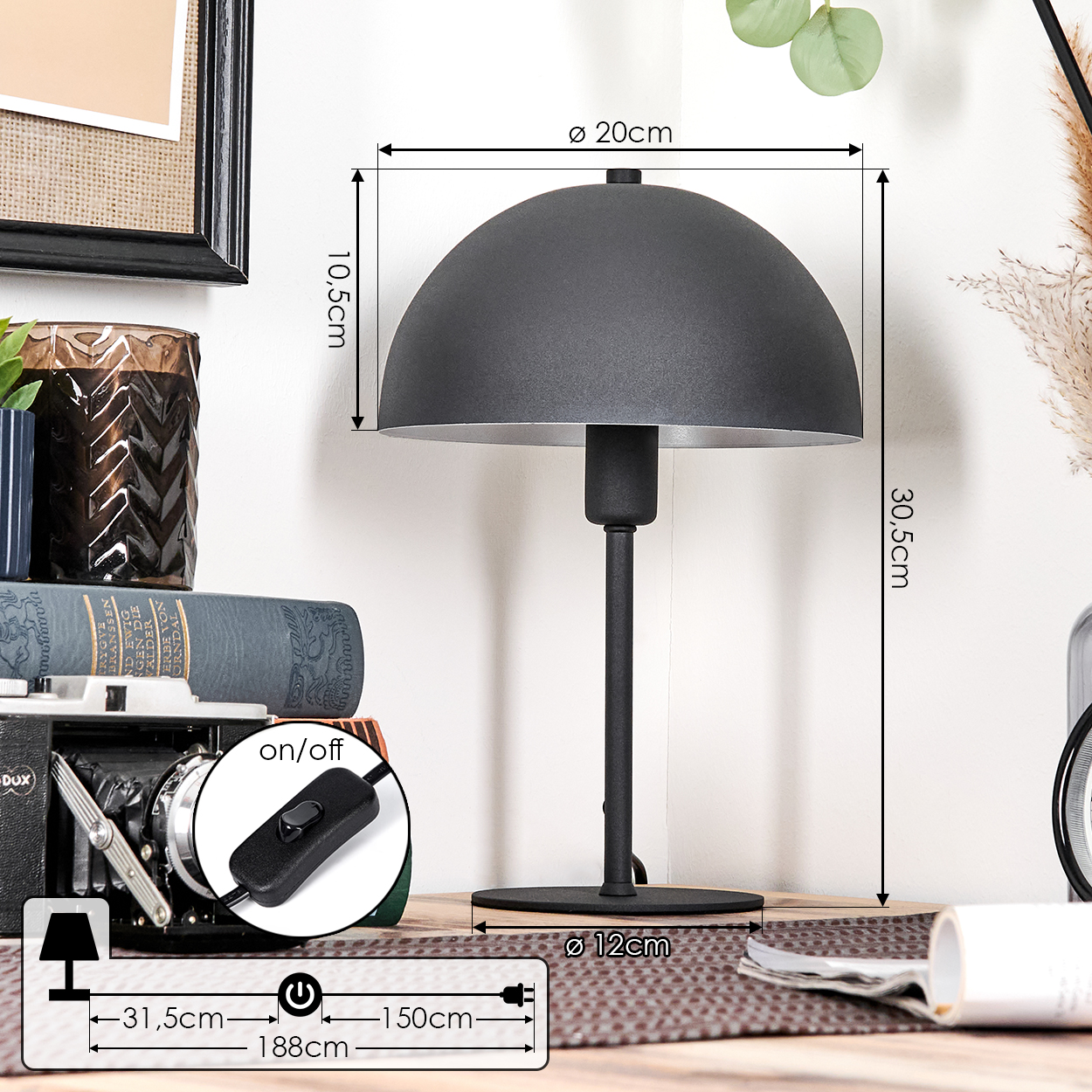 Eine schwarze Schreibtischlampe mit einem kuppelförmigen Schirm. Sie steht auf Holz, mit Büchern und einer Kamera im Hintergrund. Maße sind angegeben.
