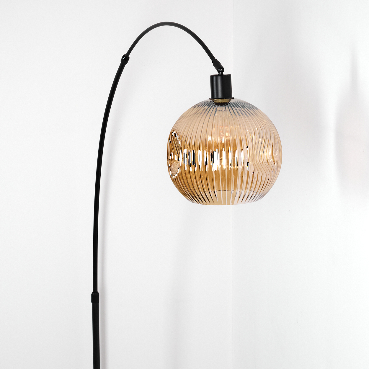 Eine moderne Stehlampe mit einem schwarzen, gebogenen Arm und einem runden, bernsteinfarbenen Glasschirm vor weißer Wand.