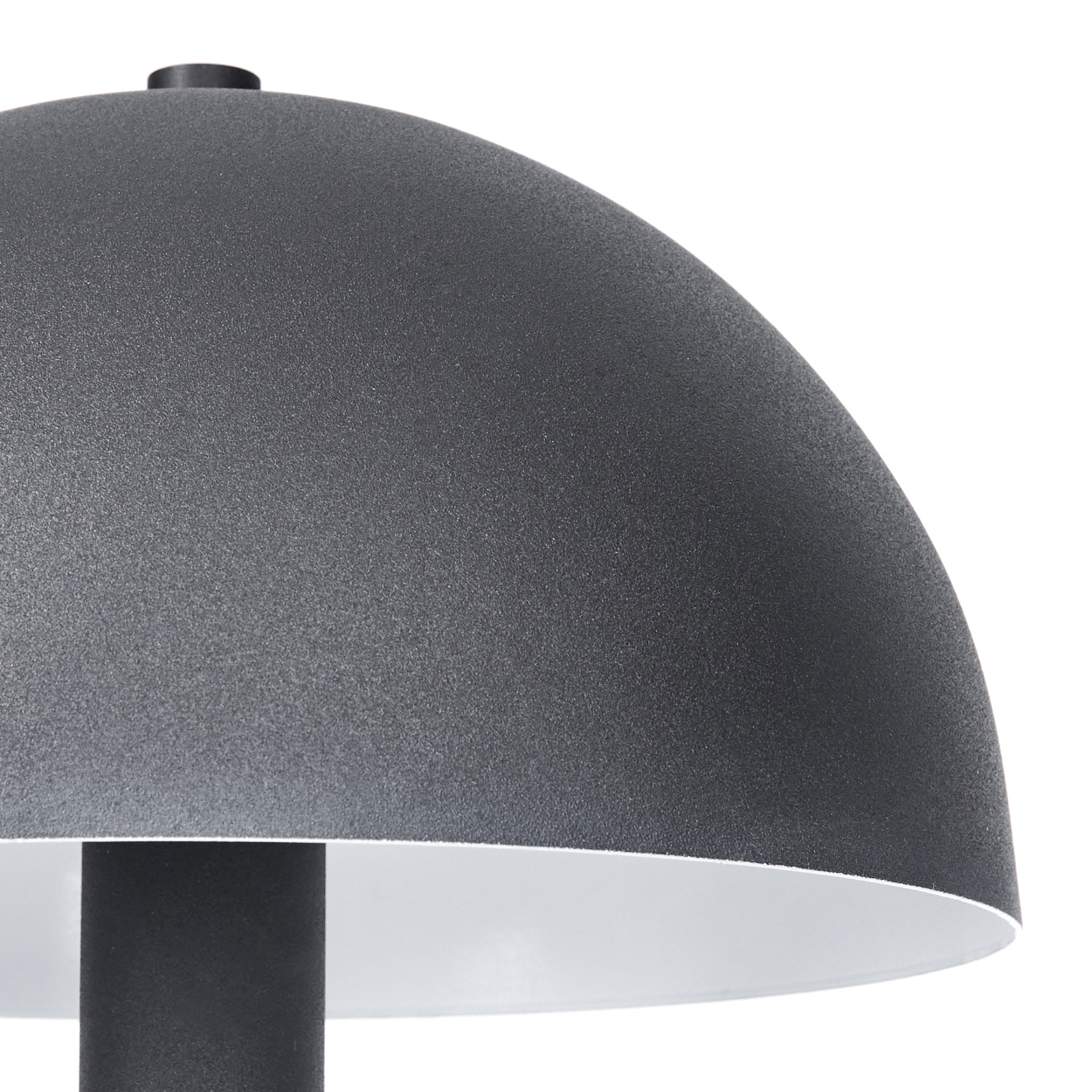 Nahaufnahme einer dunkelgrauen Lampe mit rundem Oberteil und zylindrischem Sockel. Die Innenseite der Lampe ist weiß, vor weißem Hintergrund.