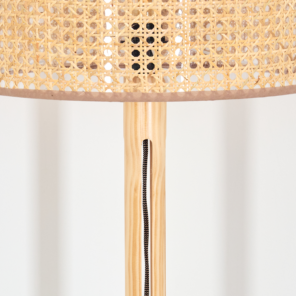 Nahaufnahme einer Lampe. Die Lampe hat einen gewebten Schirm und einen Holzständer. Ein schwarzes Kabel verläuft den Ständer hinunter.