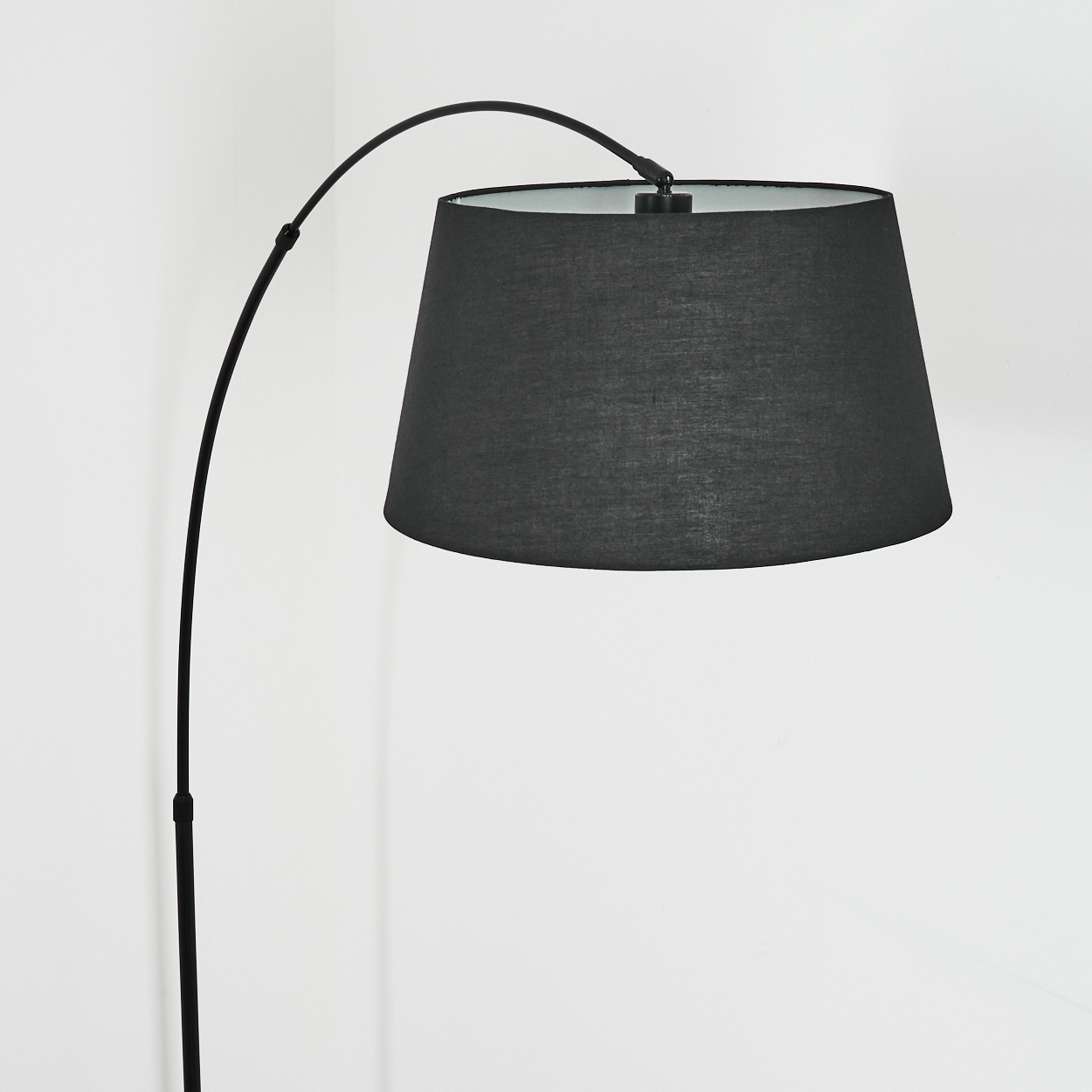 Eine moderne schwarze Bogenlampe mit großem Schirm. Die Lampe steht vor einer weißen Wand. Der Schirm ist dunkelgrau.