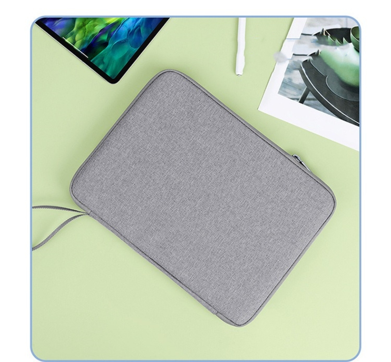 Eine graue Tablettasche auf hellgrüner Oberfläche. Tablet, Stift und ein Foto liegen daneben.