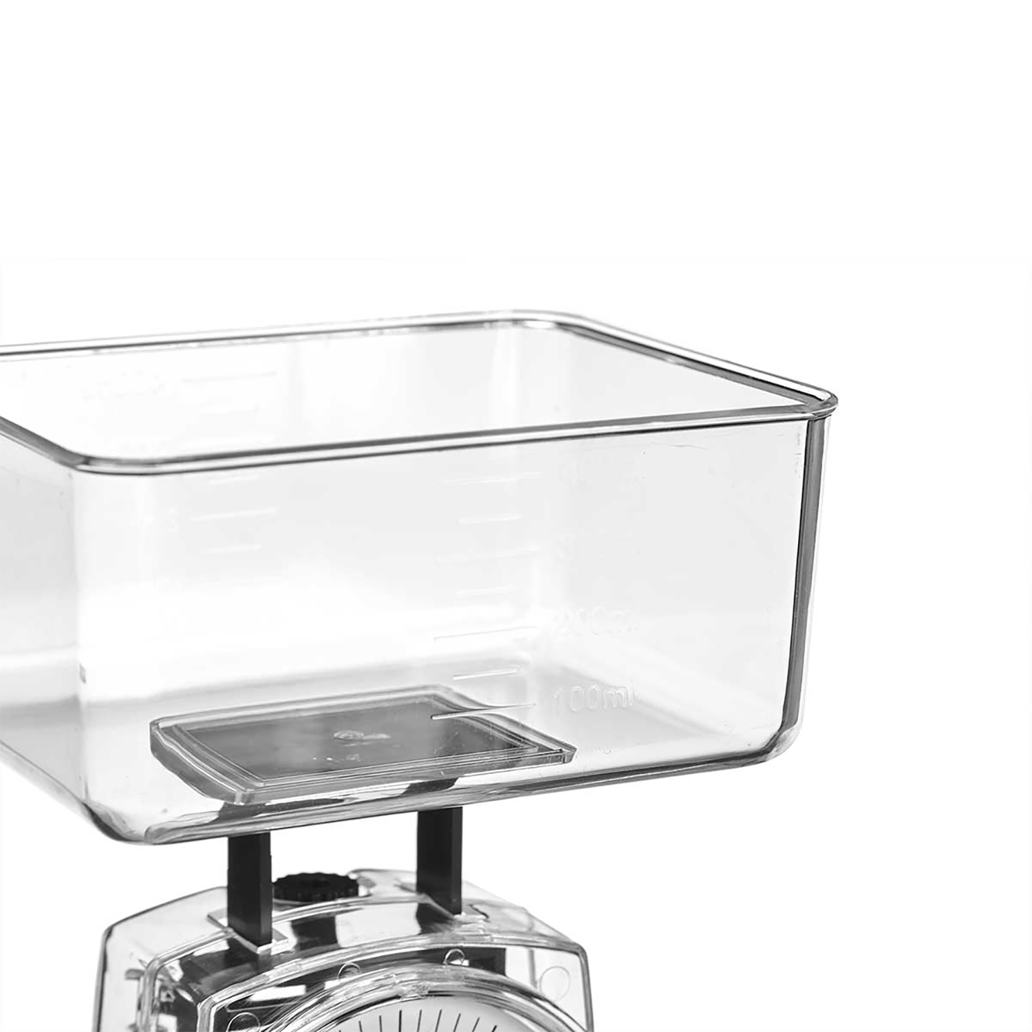 Una bilancia da cucina in plastica trasparente con un contenitore quadrato. La bilancia ha supporti neri e un quadrante. Lo sfondo è bianco.