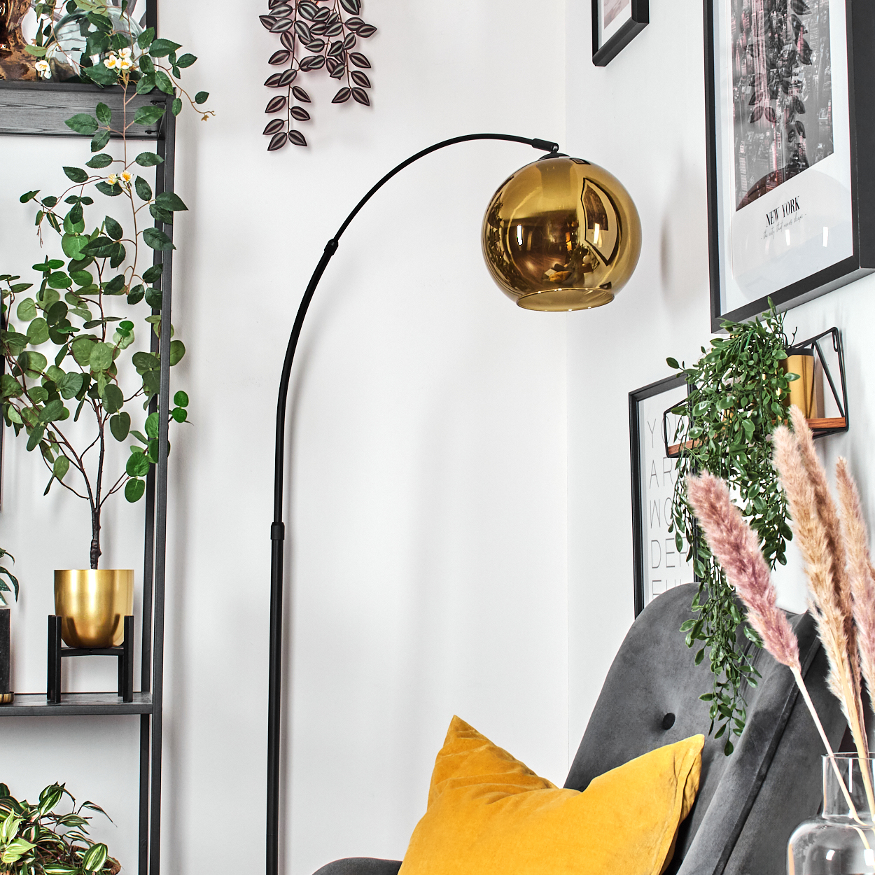 Ein Raum mit einer Stehlampe. Es gibt eine goldene Lampe, einen grauen Stuhl, ein gelbes Kissen, Pflanzen und einen schwarzen Rahmen mit einem New York-Bild.