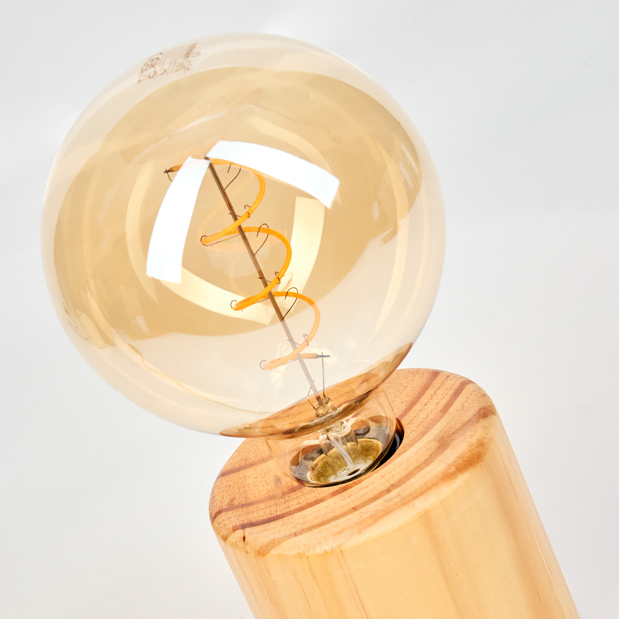 Nahaufnahme einer Glühbirne. Sie hat ein rundes, bernsteinfarbenes Glas mit einem Glühfaden. Sie sitzt auf einem Holzsockel.
