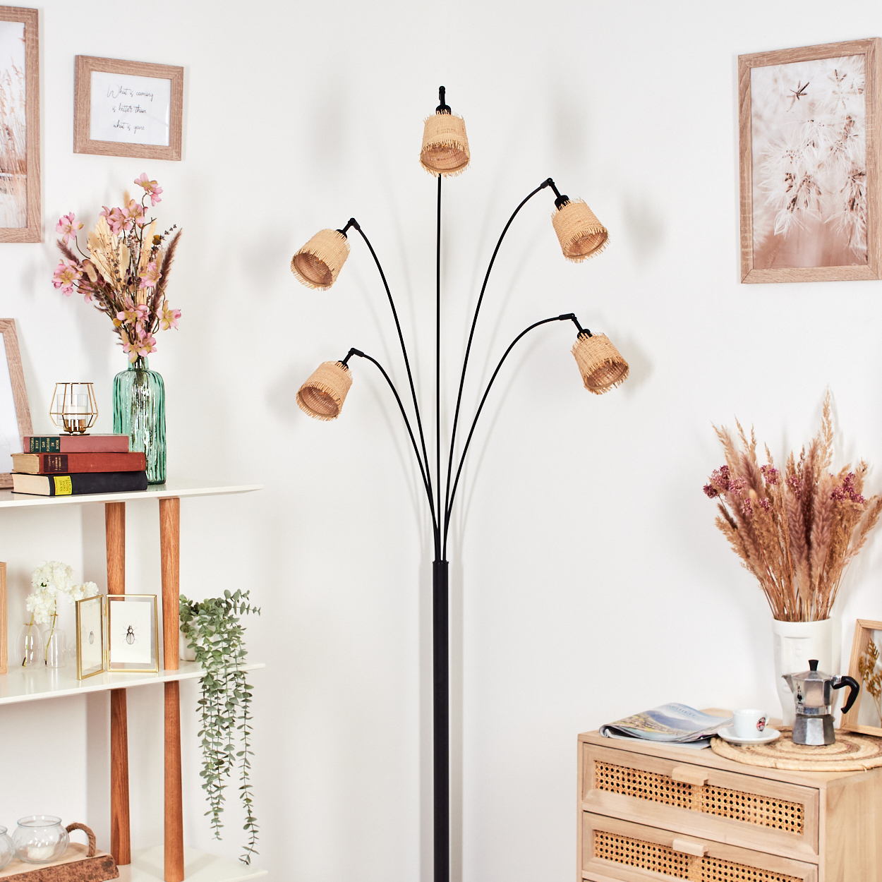 Eine Stehlampe mit fünf gewebten Lampenschirmen steht in einem Raum mit weißer Wand. Regale und ein Schrank sind ebenfalls zu sehen.