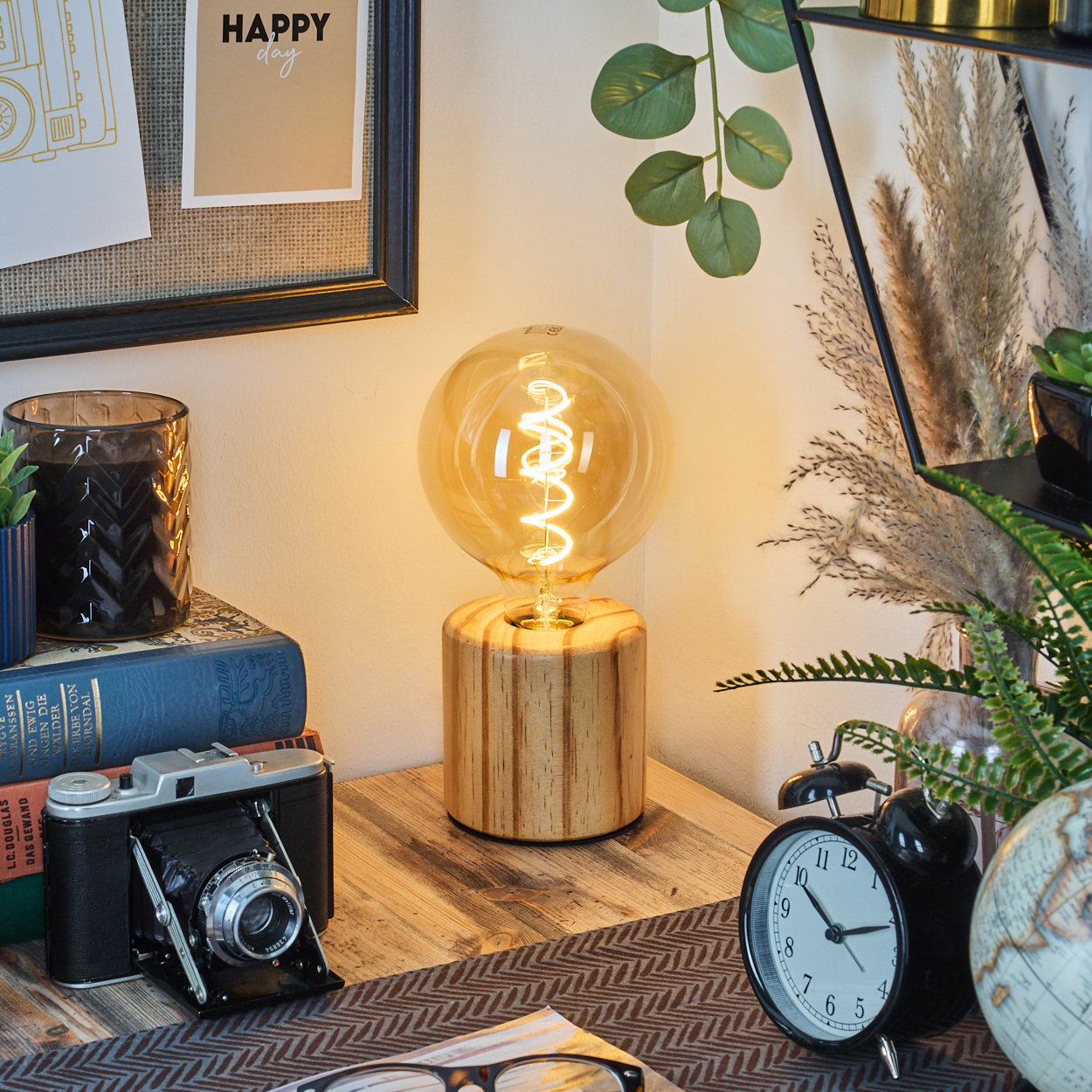 Eine leuchtende Glühbirnenlampe auf einem Holzsockel. Kamera, Bücher, Uhr und Pflanzen auf einem Tisch. Happy-Day-Poster.