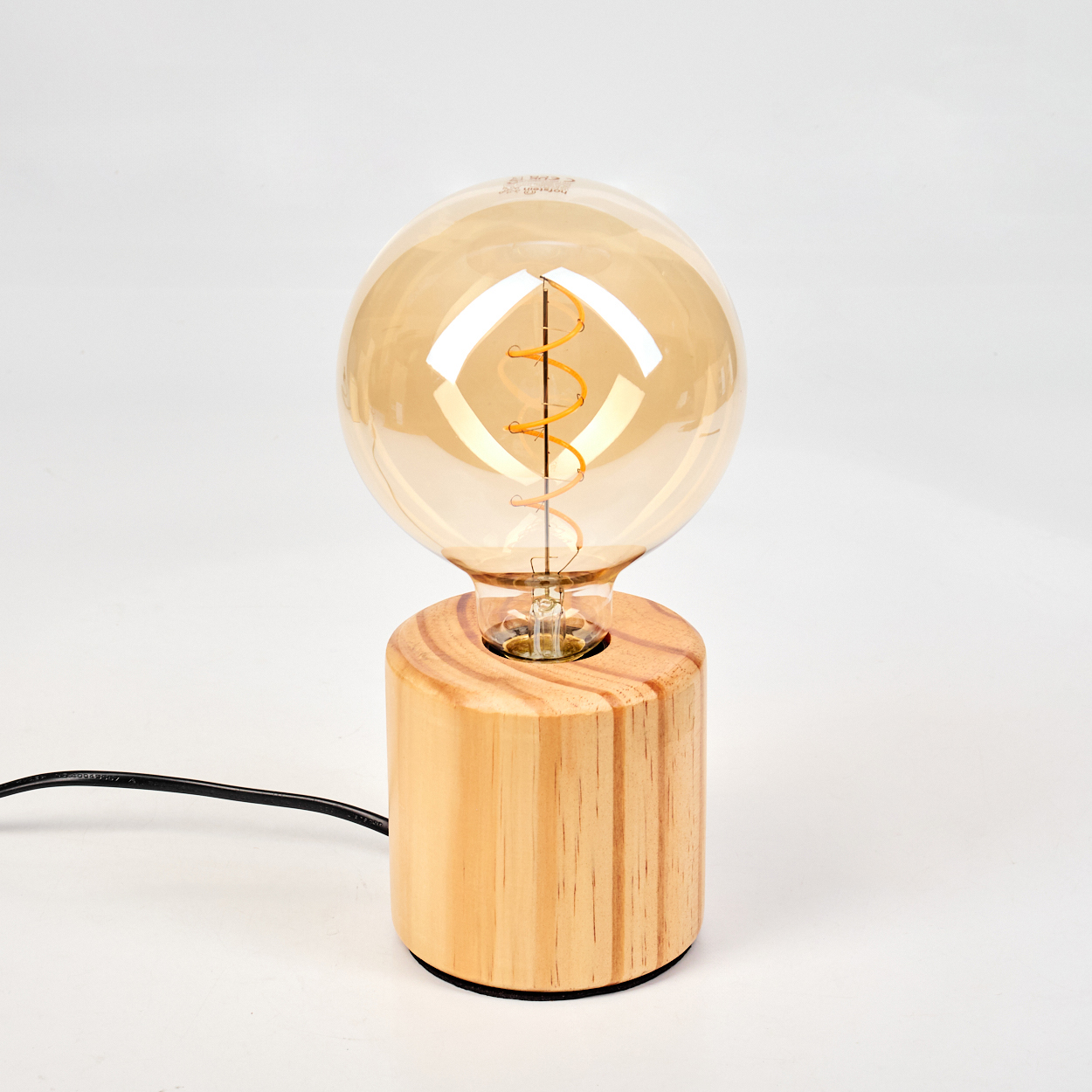Eine dekorative Lampe mit einer großen, runden, bernsteinfarbenen Glühbirne und einem Holzsockel. Schwarzes Kabel.