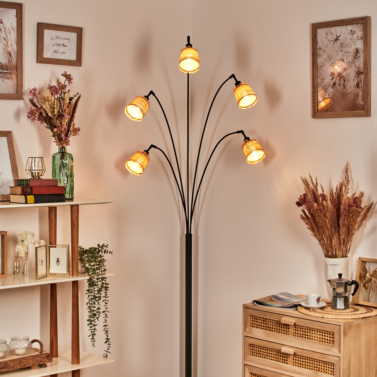 Eine Stehlampe mit fünf Lichtern. Es gibt einen Holzschrank, eine Vase mit Blumen und gerahmte Bilder an der Wand.
