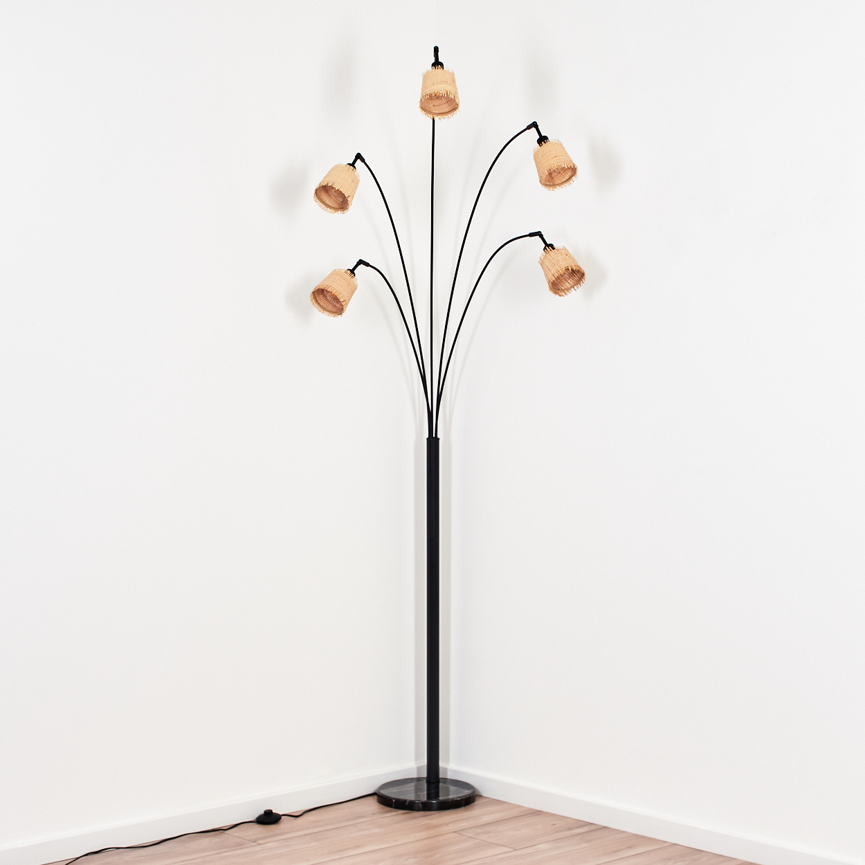 Eine Stehlampe mit sechs gewebten Lampenschirmen. Die Lampe ist schwarz mit einem Marmorsockel, vor weißen Wänden und Holzboden.