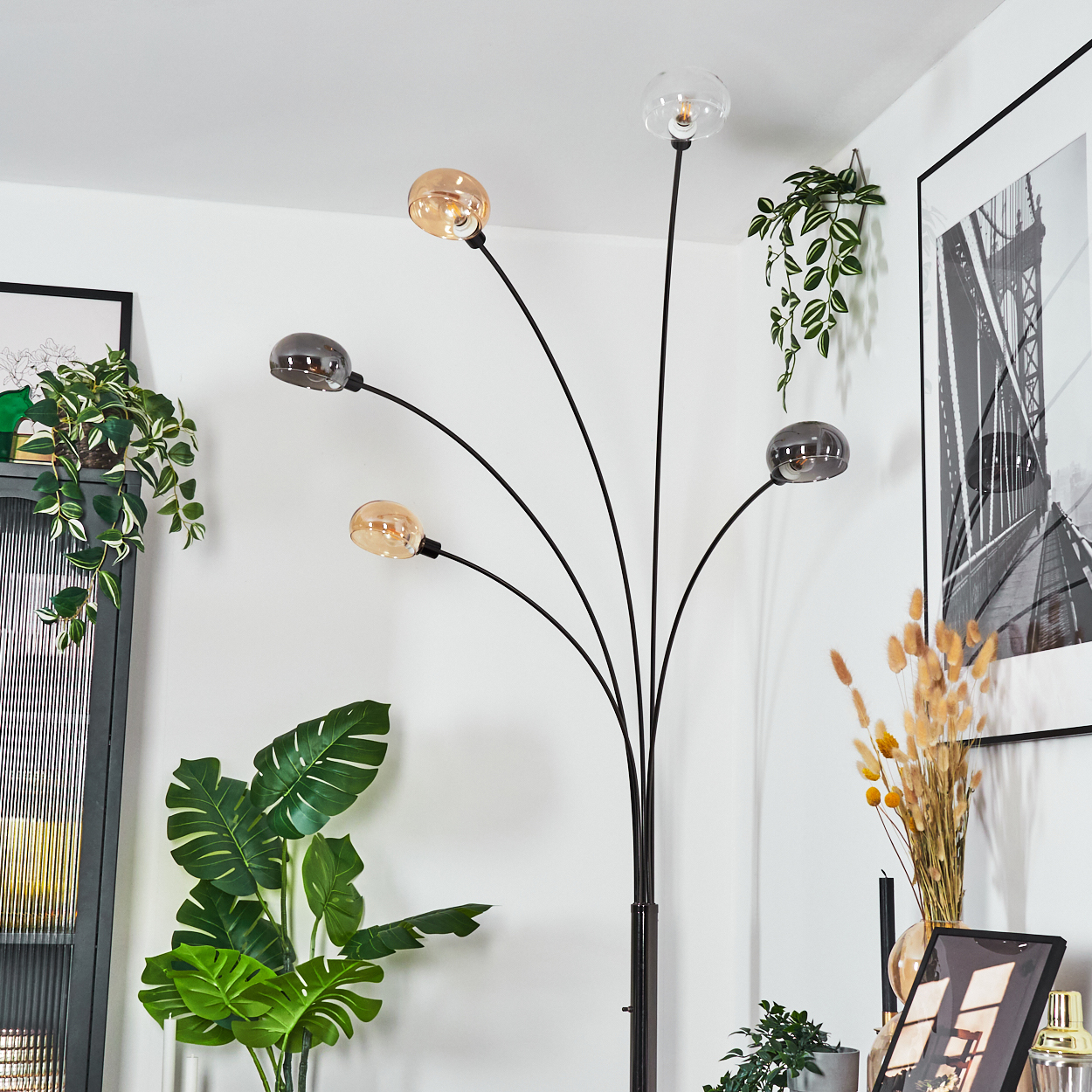 Eine moderne Stehlampe mit fünf Glühbirnen, Pflanzen und einem schwarz-weiß gerahmten Bild in einem weiß getäfelten Raum.