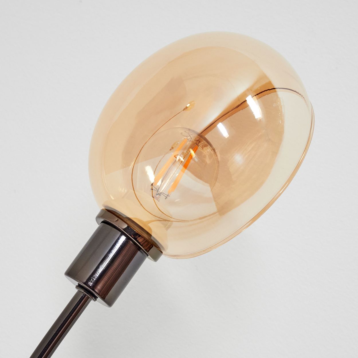 Nahaufnahme einer dekorativen Glühbirne mit braunem Glas. Die Glühbirne ist an einem dunklen Metallarm vor weißem Hintergrund befestigt.