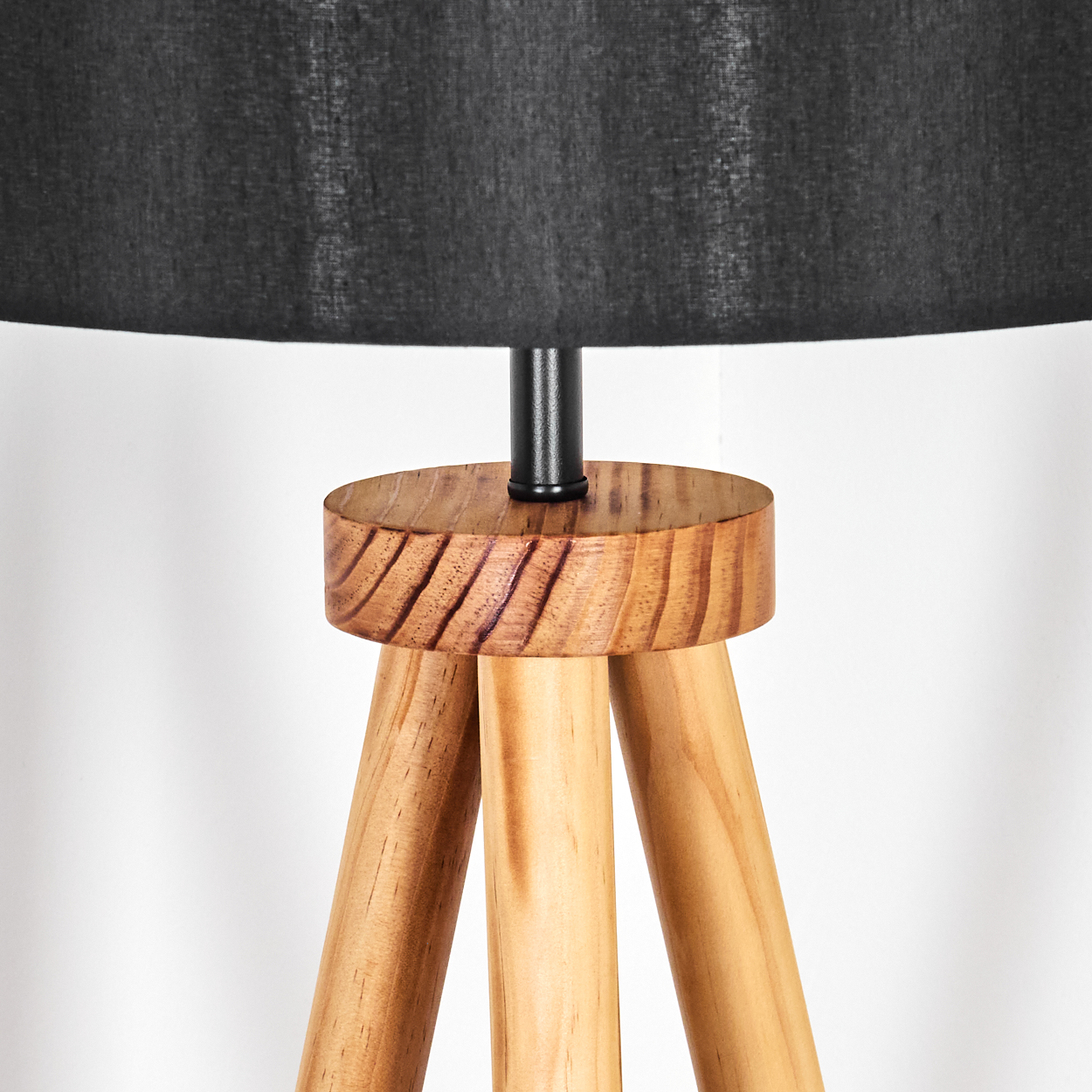 Eine hölzerne Stativlampe mit schwarzem Lampenschirm. Das Stativ ist hellbraun, der Schirm dunkel.