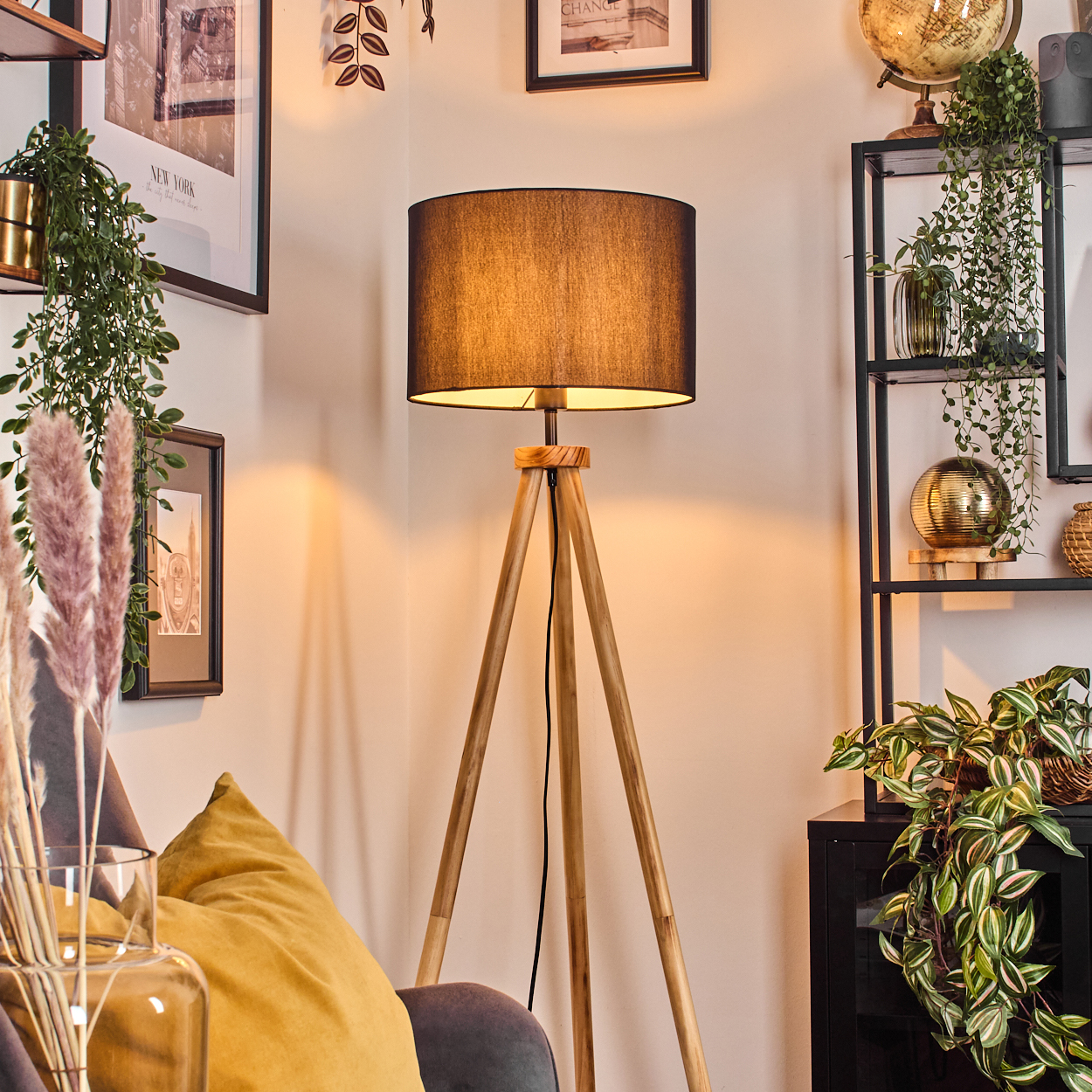 Ein modernes Wohnzimmer mit einer Holzstativlampe, Pflanzen, einem Globus und gerahmten Bildern an der Wand.