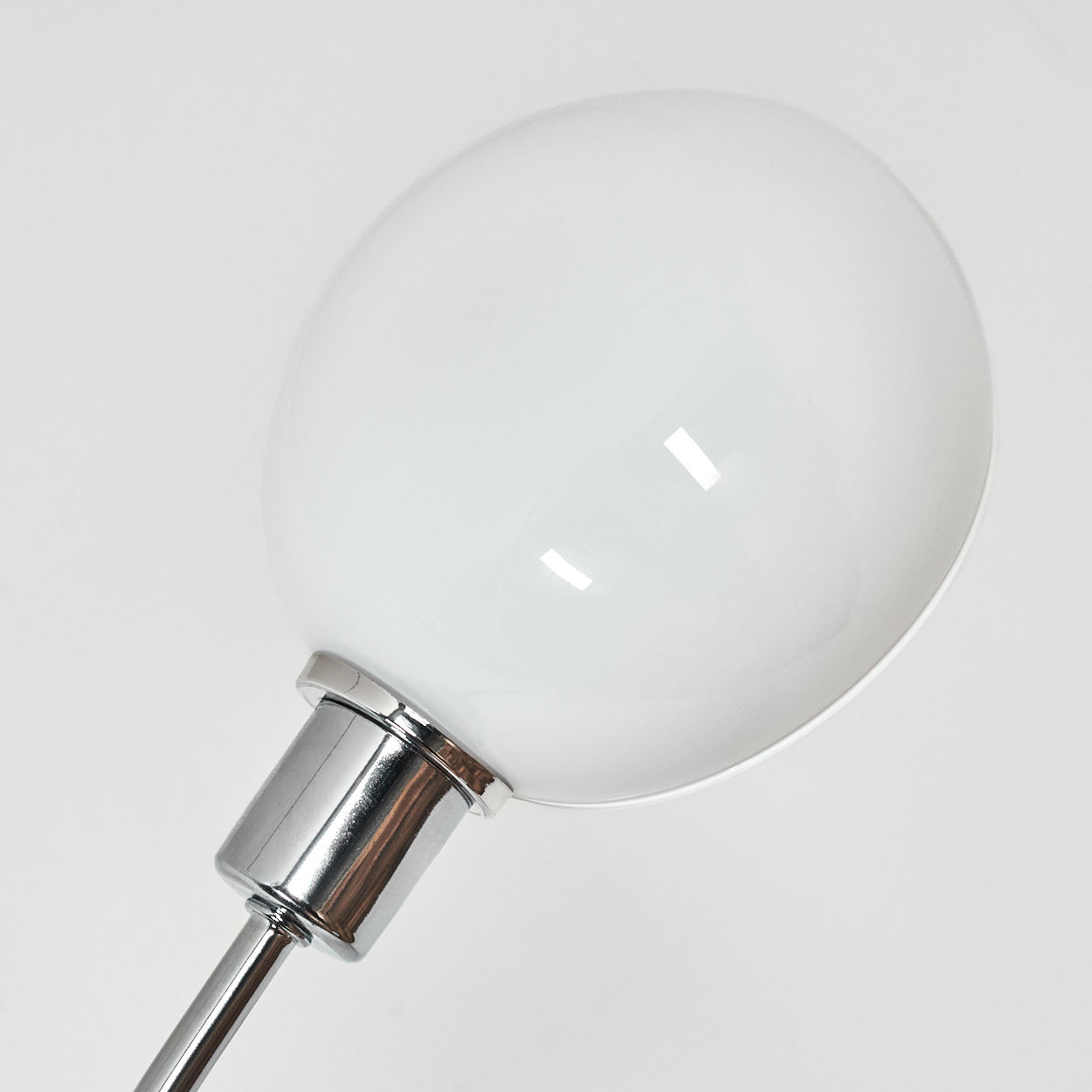 Nahaufnahme einer weißen Lampe mit Chromfuß. Die Lampe hat einen großen, abgerundeten Schirm. Der Hintergrund ist weiß.