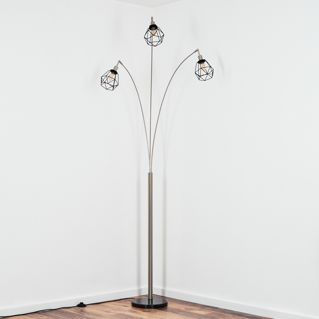 Eine moderne Stehlampe mit drei Lichtern. Sie hat schwarze, geometrische Schirme und einen silbernen Mast. Sie steht in einer Ecke mit weißen Wänden und Holzboden.