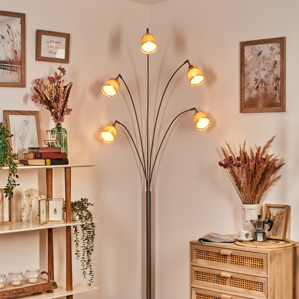 Eine Zimmerecke mit Stehlampe, Kunst, Regalen mit Deko und einem Holzschrank. Trockenblumen, Bücher und Kerzen sind sichtbar.