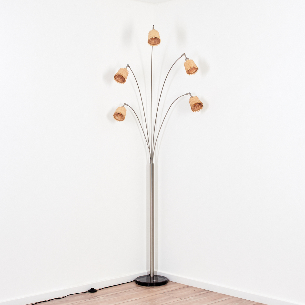 Eine Stehlampe mit fünf Lampenschirmen. Die Lampe steht in einer Ecke eines Raumes mit weißen Wänden und Holzboden.