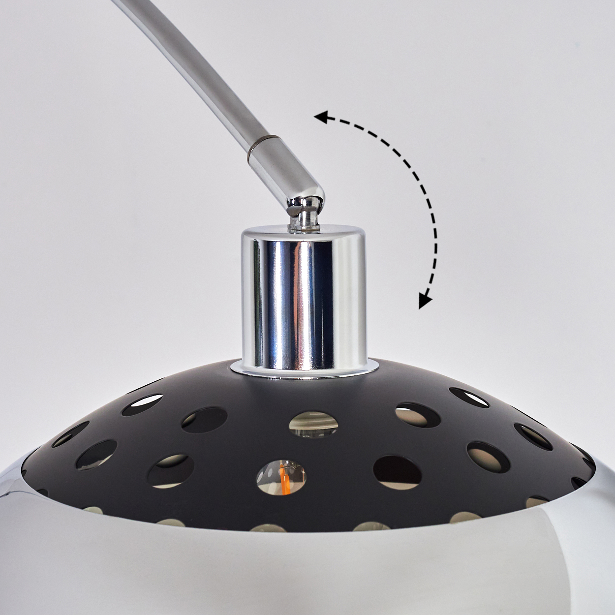 Nahaufnahme einer Lampe. Die Lampe hat einen schwarzen Schirm mit Löchern und einen Chromfuß. Ein Chromarm erstreckt sich nach oben.