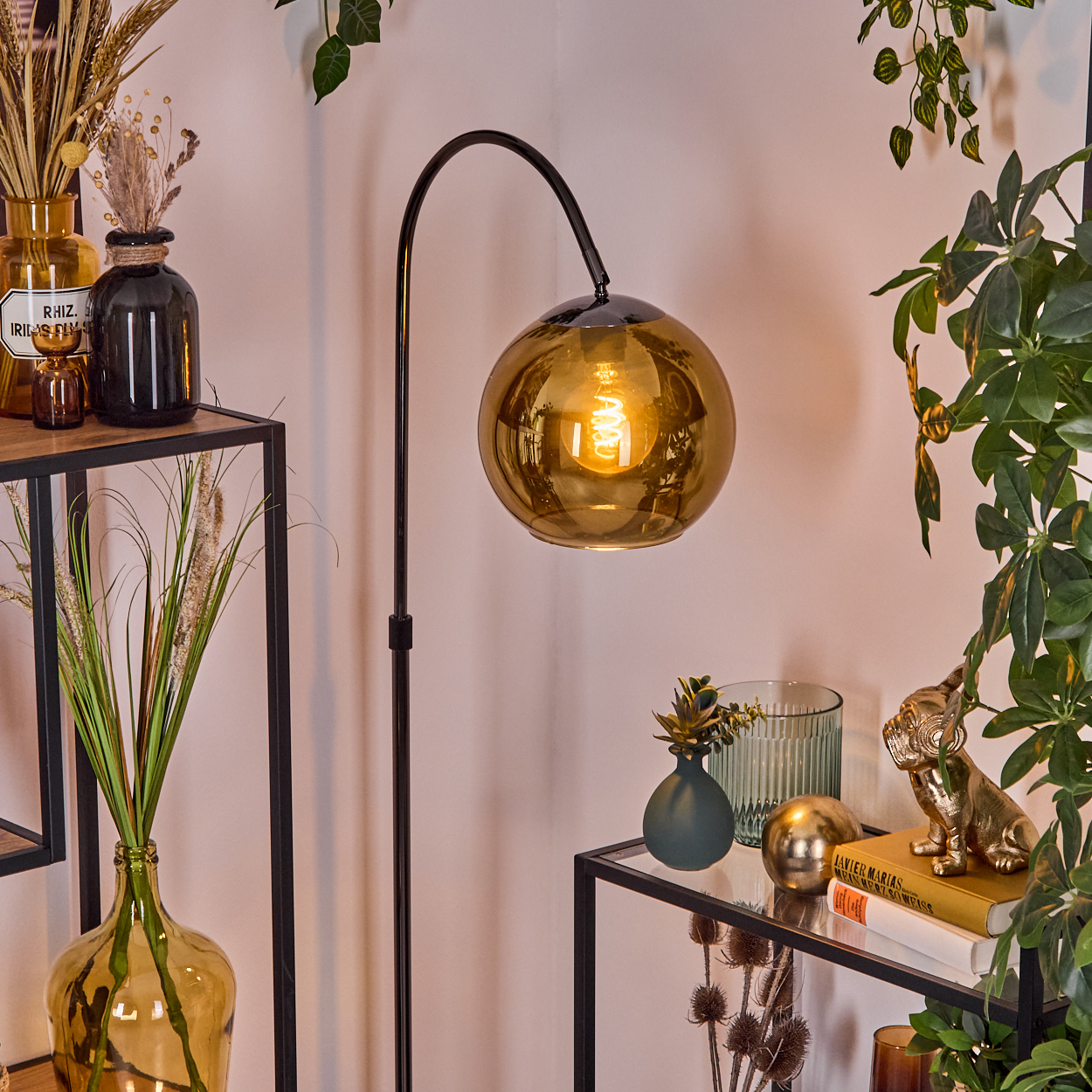 Modernes Wohnzimmer mit schwarzer Lampe, dekorativen Vasen, Pflanzen und Regalen. Eine goldene Kugellampe steht im Mittelpunkt.