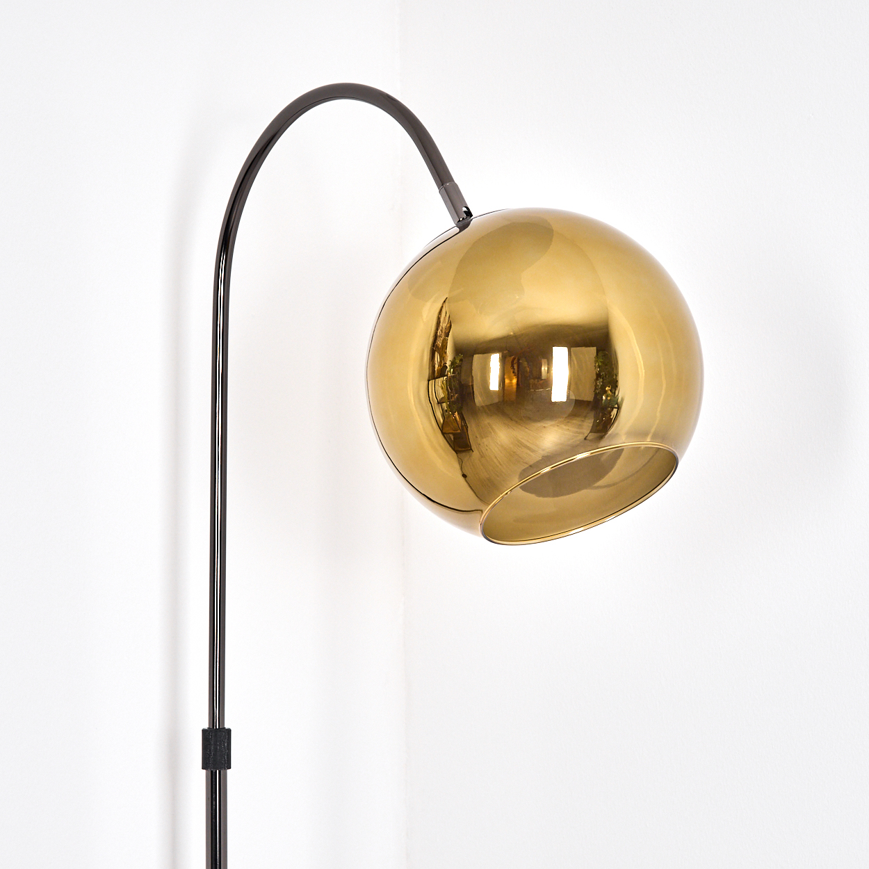 Eine moderne Stehlampe mit goldenem Kugelschirm und schwarzem Rahmen steht in der Ecke eines weißen Raumes.